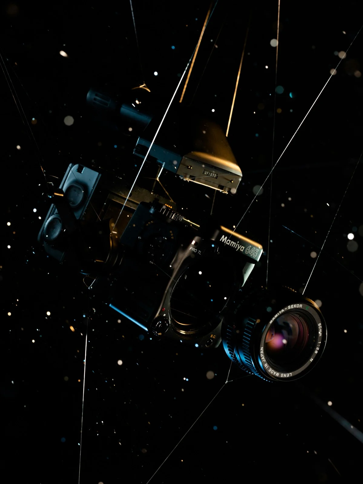 Disassembled Mamiya 645 medium format camera body and 80mm lens floating against a starry black background