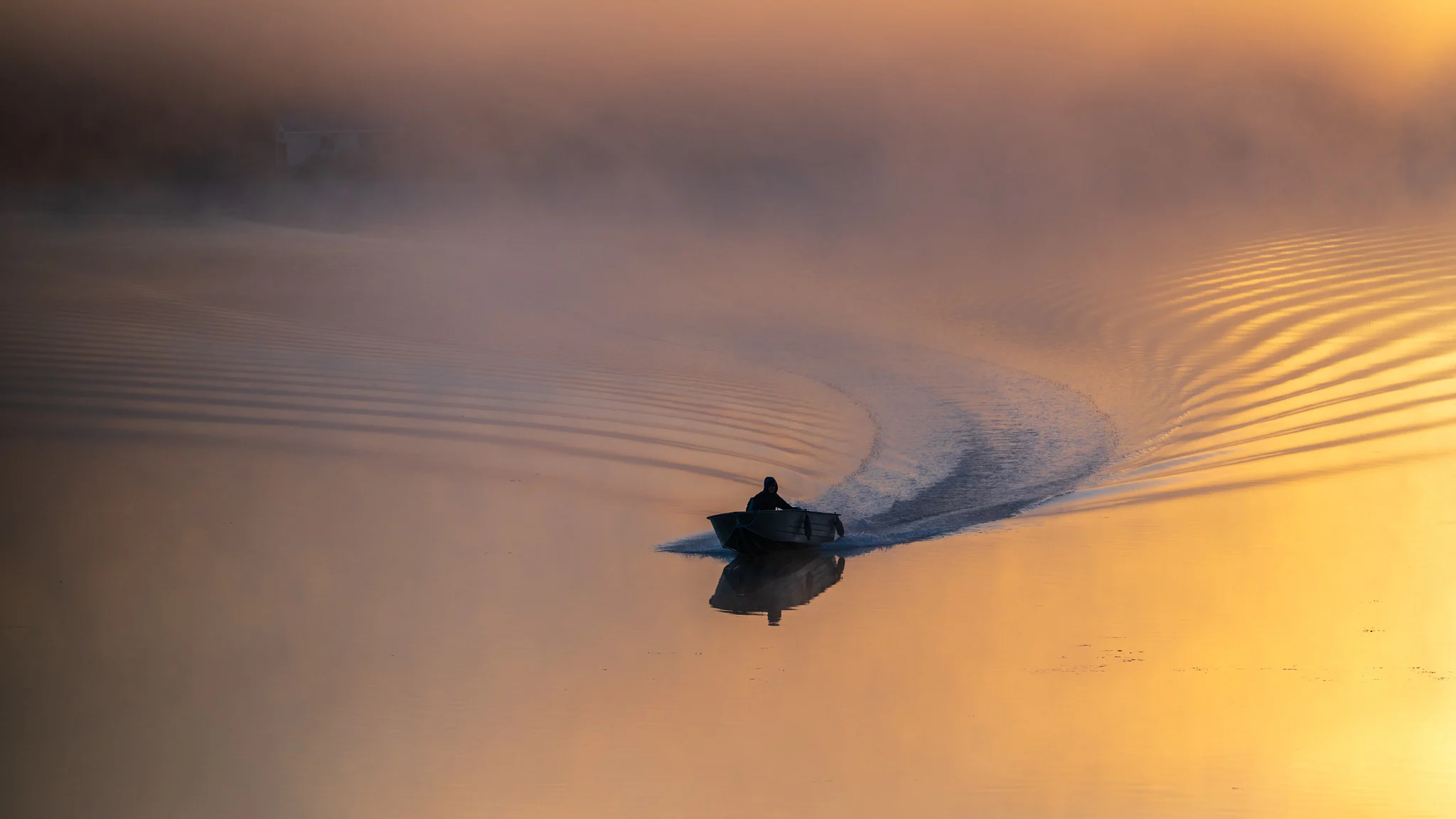Small boat silhouetted on misty water at sunrise, backlit by low sun so the wake and mist glow warm gold around the dark silhouette