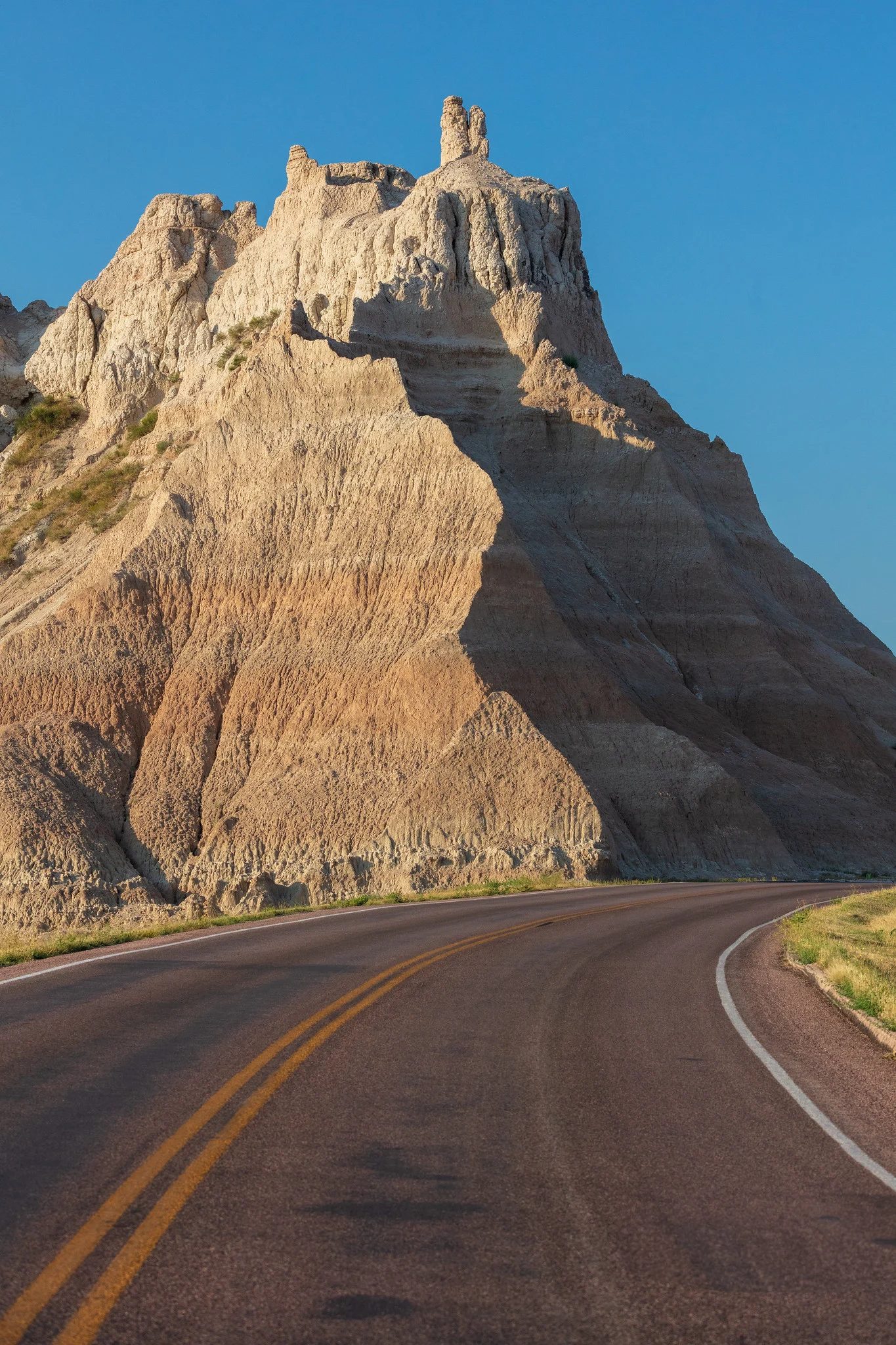 Sun-carved badlands butte lit from the side at low sun angle, with strong vertical shadow lines showing erosion texture down the rock face