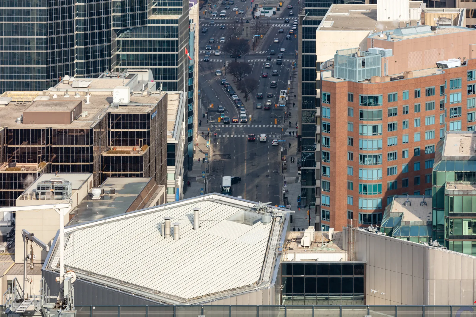 A wide downtown avenue seen from high above, running between office towers and rooftops, with traffic and crosswalks far below