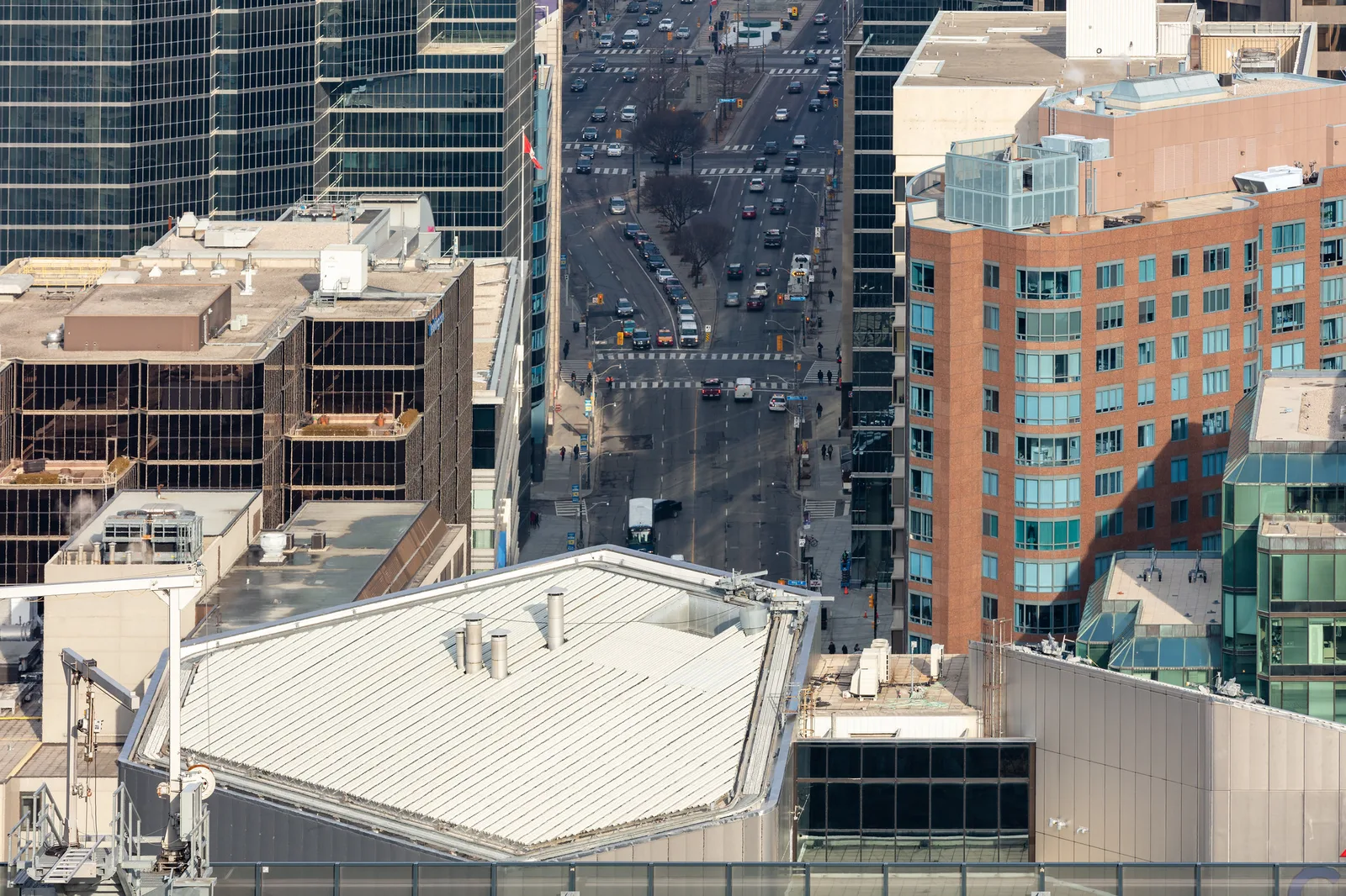 A straight city avenue seen from a high vantage point between office buildings, with several blocks of traffic and crossings stacked up the frame