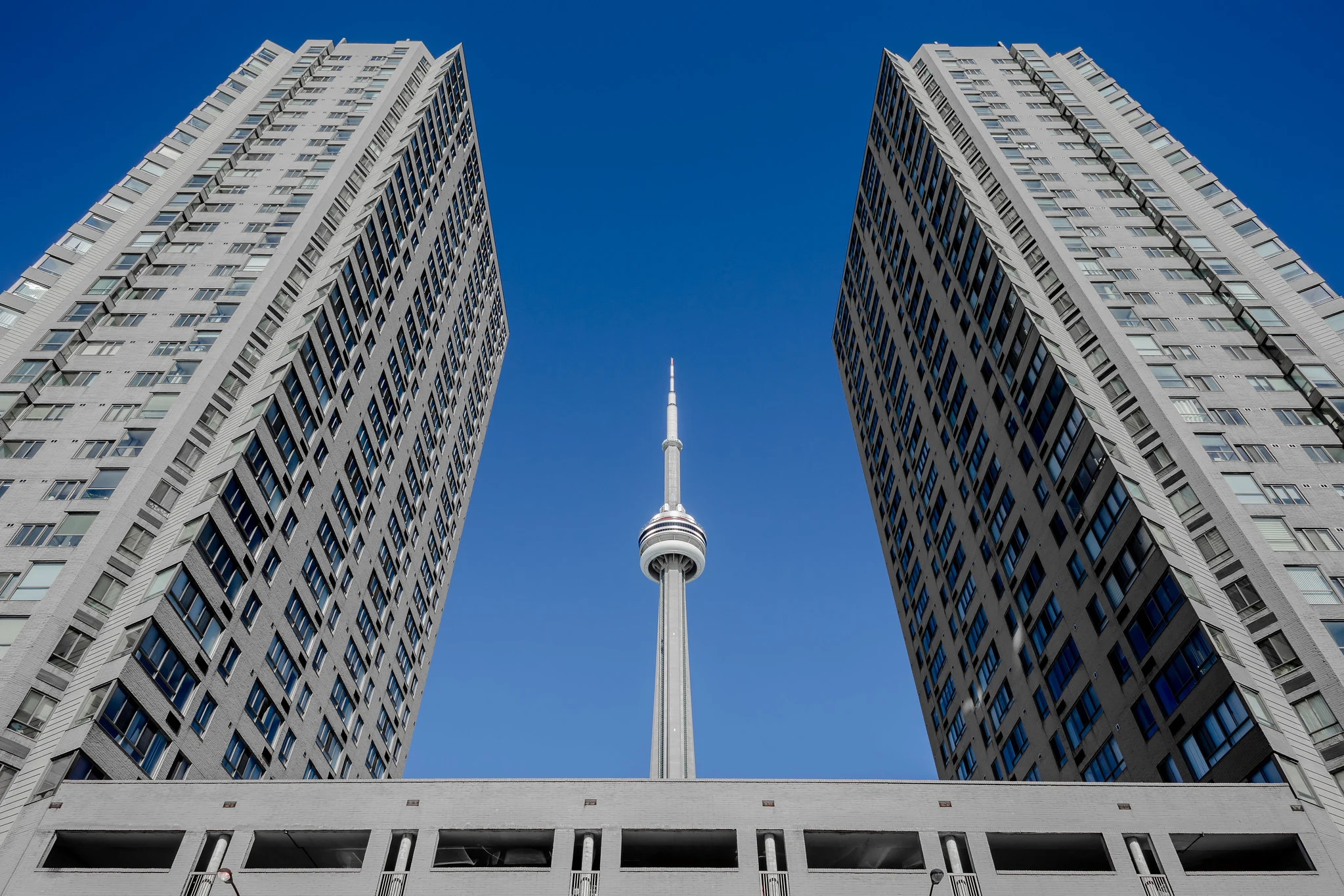 Two nearly identical apartment towers framing the CN Tower symmetrically between them against a clear blue sky