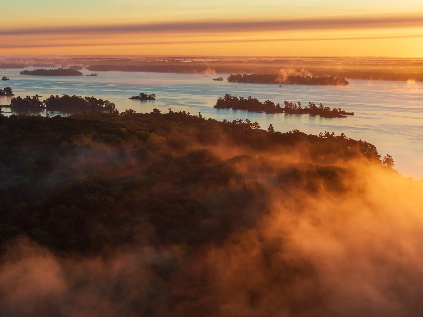 Aerial view of a foggy river landscape at sunrise with islands emerging from low haze and warm golden light