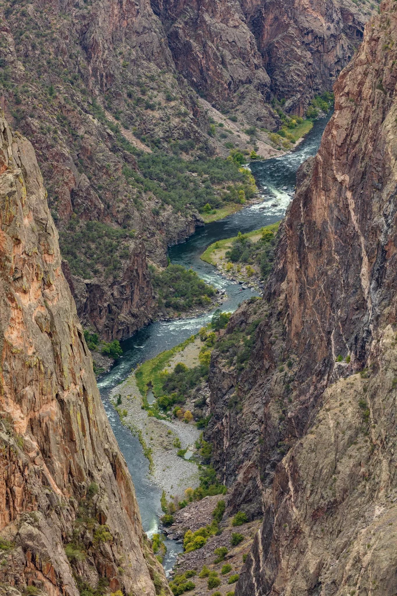 Looking down into a deep, narrow canyon with steep rocky walls and a green river winding along the bottom