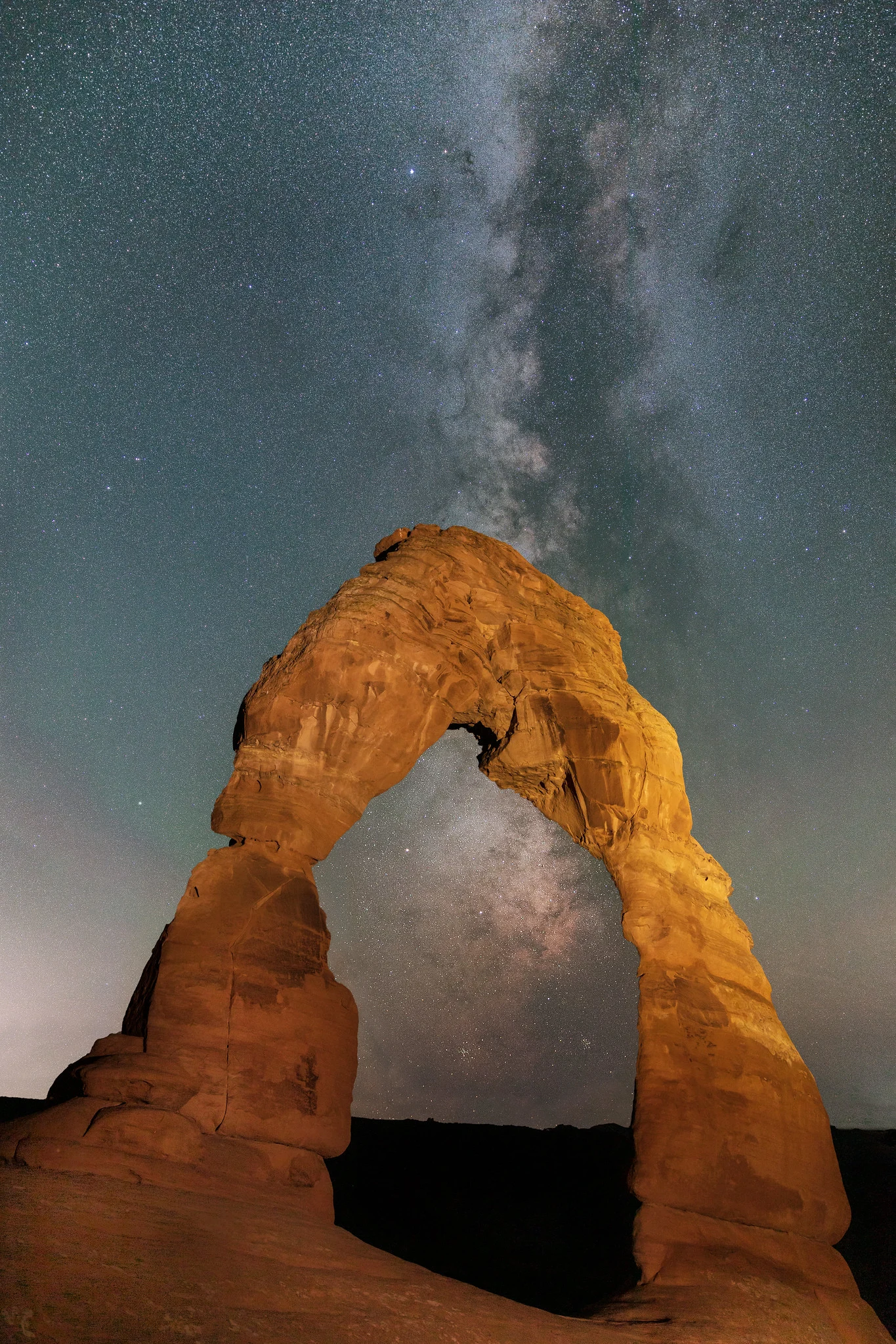 Delicate Arch in Utah silhouetted against a vertical composition with the Milky Way core rising directly above it