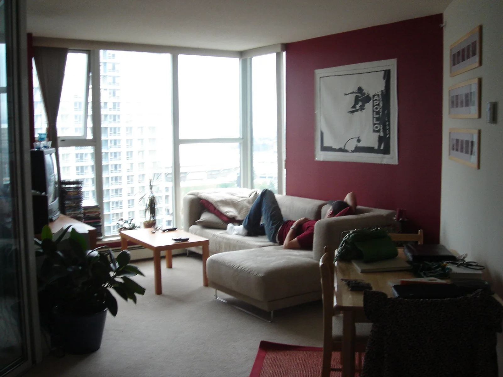 A living room with a large framed print hung above a sofa on a dark red wall, three small matching frames stacked in a column on the side wall, and floor-to-ceiling windows