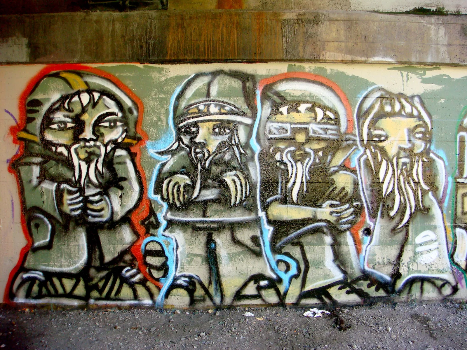 A row of four painted bearded figures in helmets on a concrete wall beneath an overpass, with gravel along the bottom