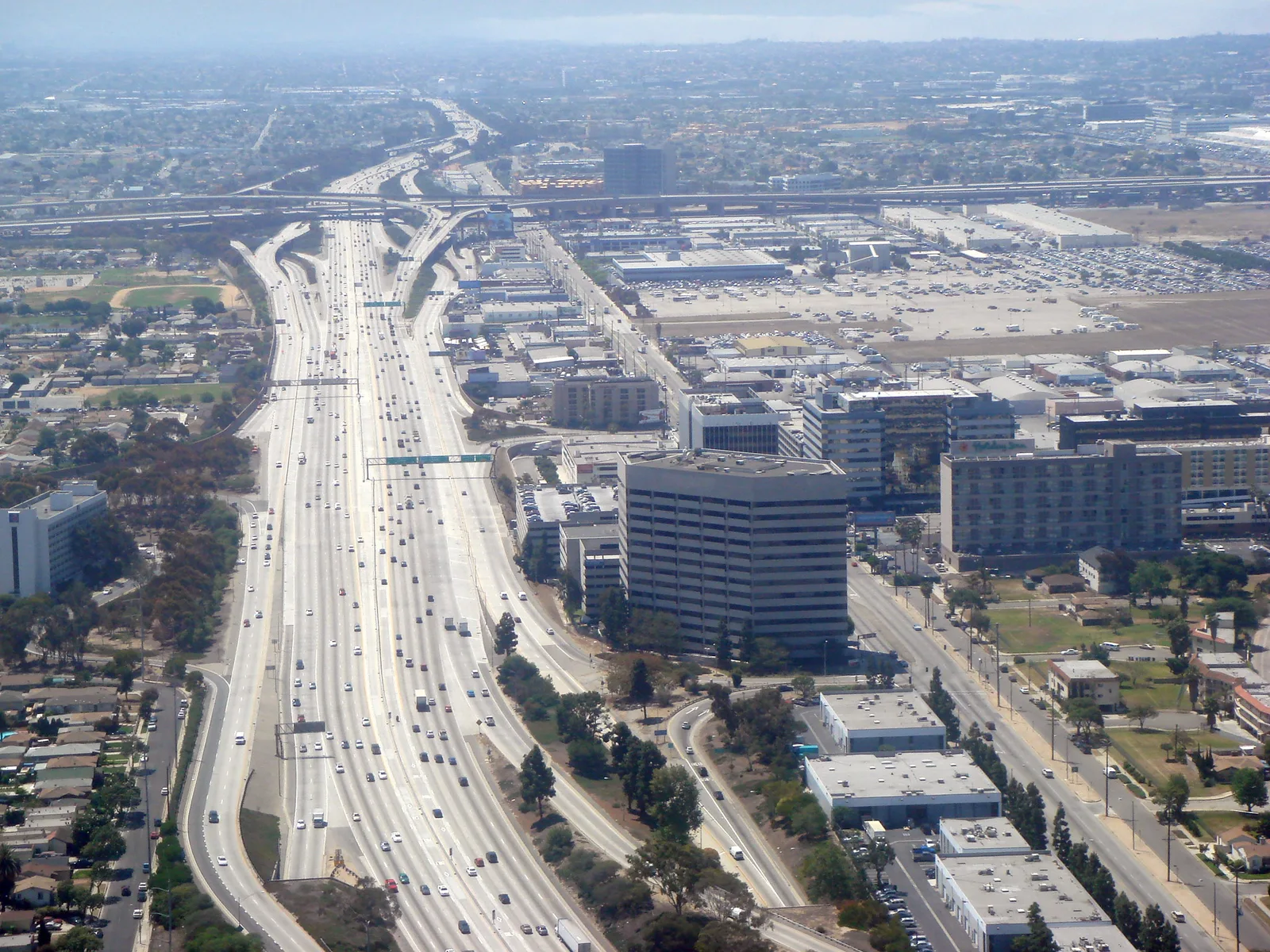 An aerial view of a wide freeway running through a city of office blocks and suburbs, with the far districts fading into pale grey haze
