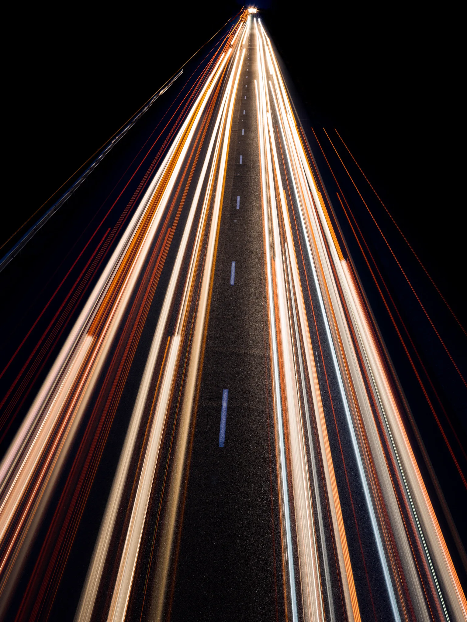 Long streaks of white and red vehicle lights along a straight multi-lane highway at night, seen from above and converging toward the top of a vertical frame