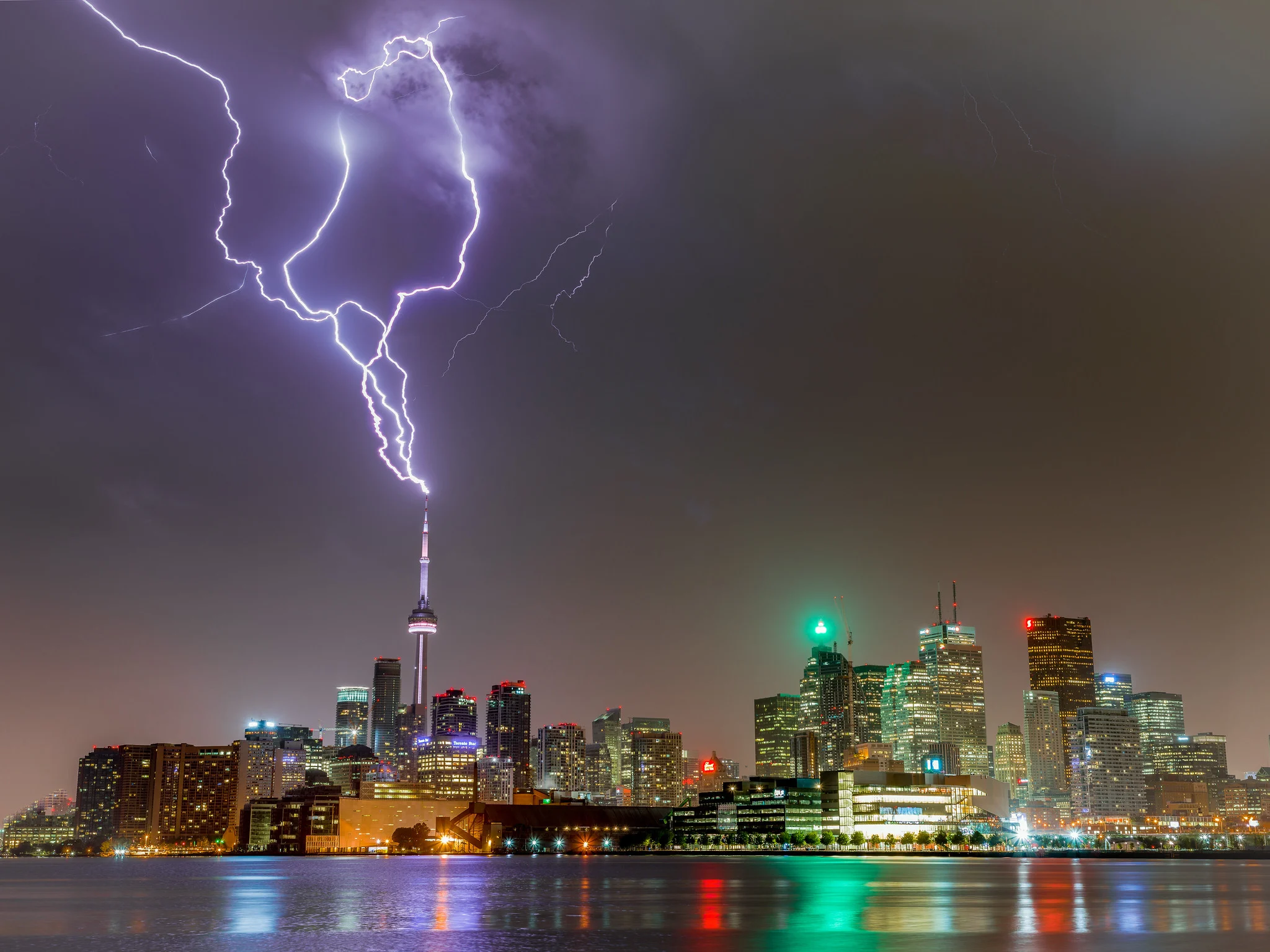 A long exposure capturing a lightning bolt striking the CN Tower in Toronto against a stormy night sky