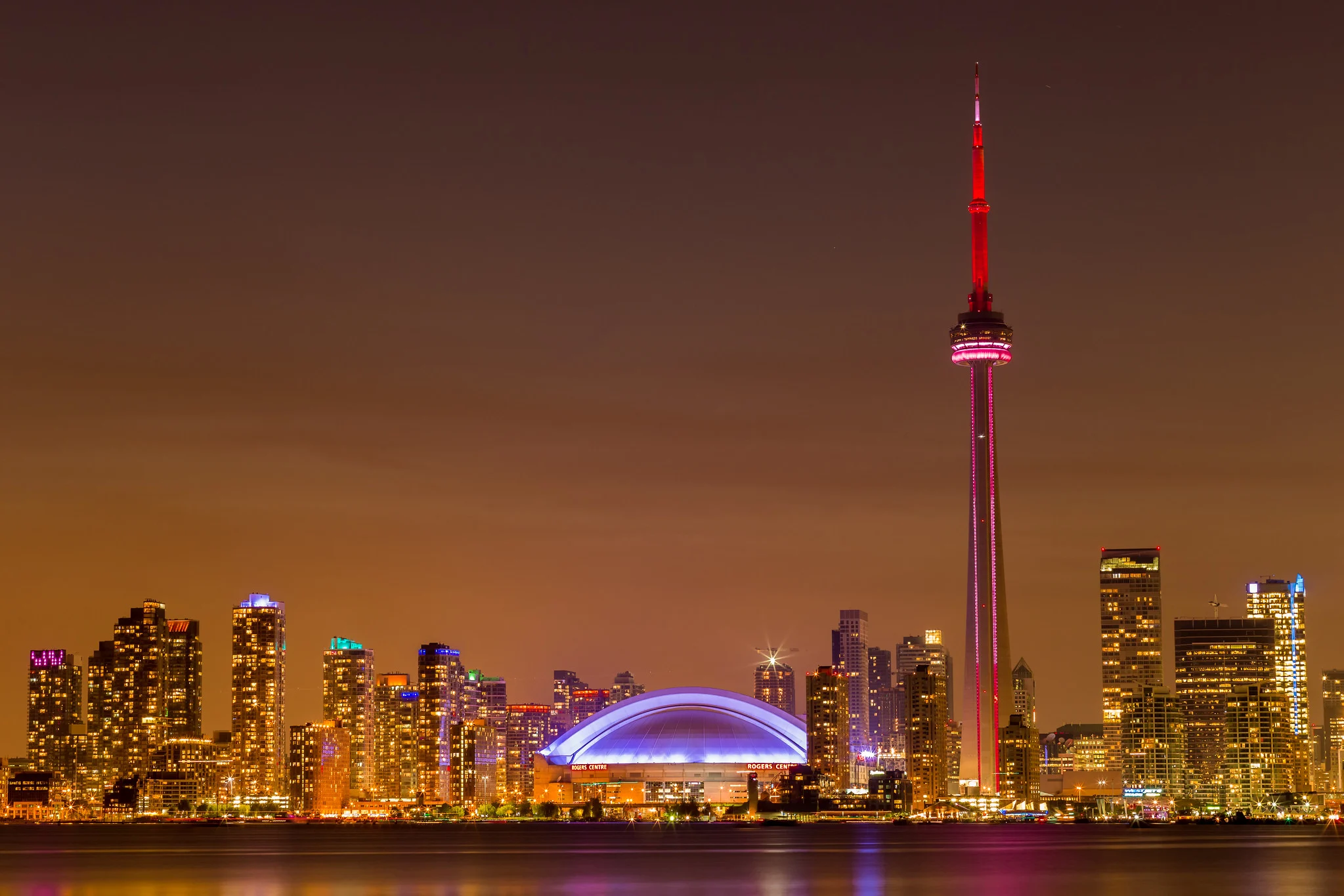 The Toronto skyline and CN Tower at night, with the water in the foreground smoothed by a long exposure