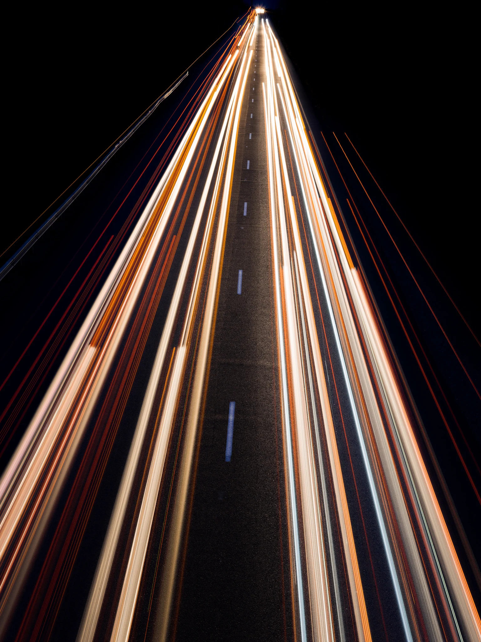 A straight highway at night with headlight and taillight trails from passing trucks converging toward the horizon