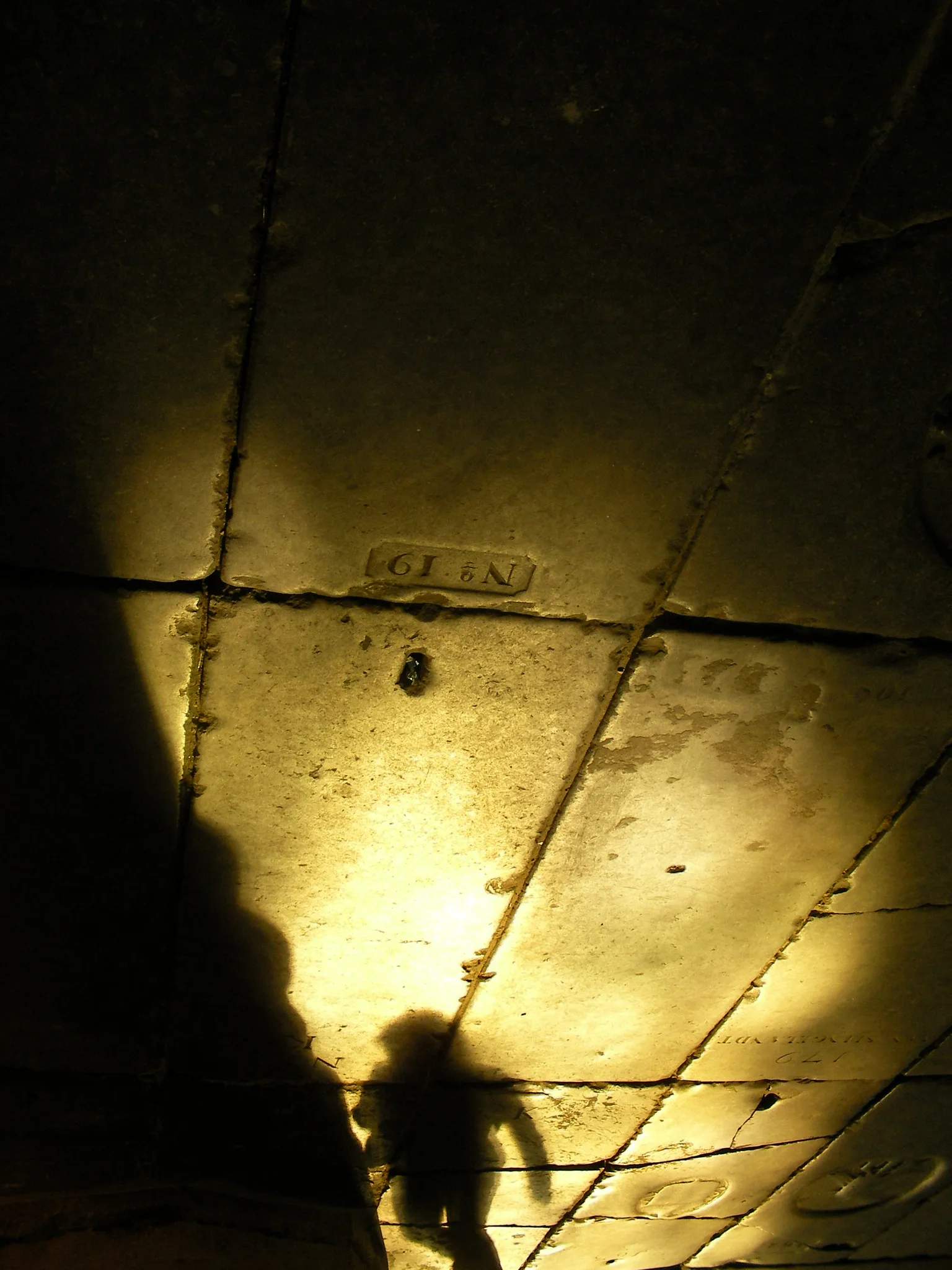 A figure's shadow falling on worn stone paving inside a pool of warm light, surrounded by darkness