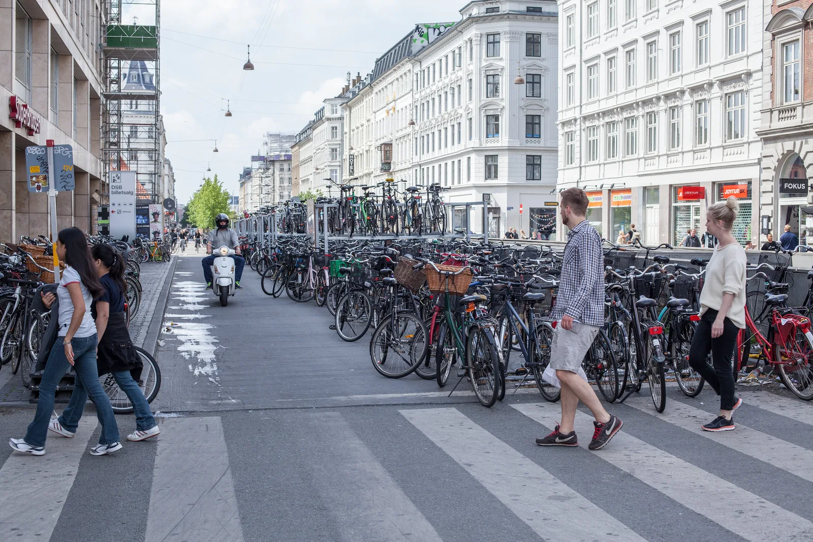 Pedestrians walking in both directions over a zebra crossing in a city street lined with rows of parked bicycles