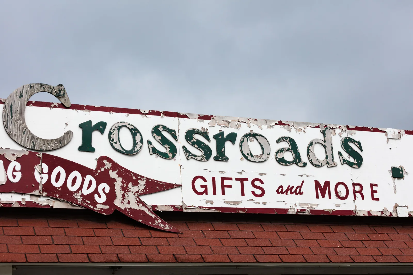 Close view of an old roadside shop sign with green and red lettering on white, the paint chipped and flaked away in patches