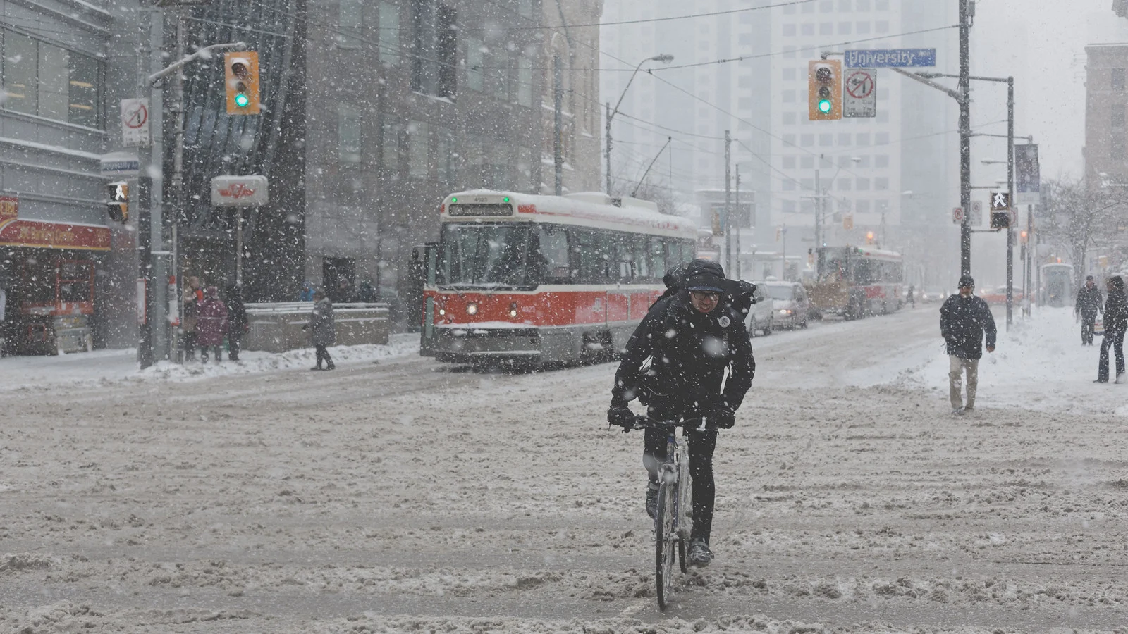 A cyclist riding through a heavy snowstorm on a city street with a streetcar behind them