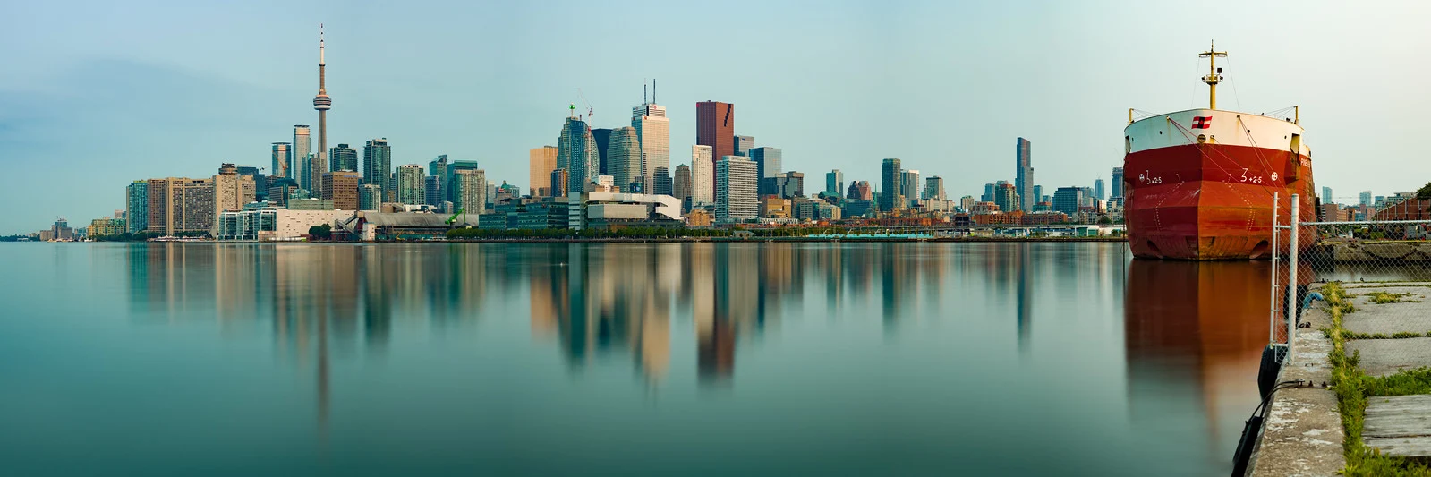 The same Toronto skyline at calm, still dawn with a ship reflected in glassy water