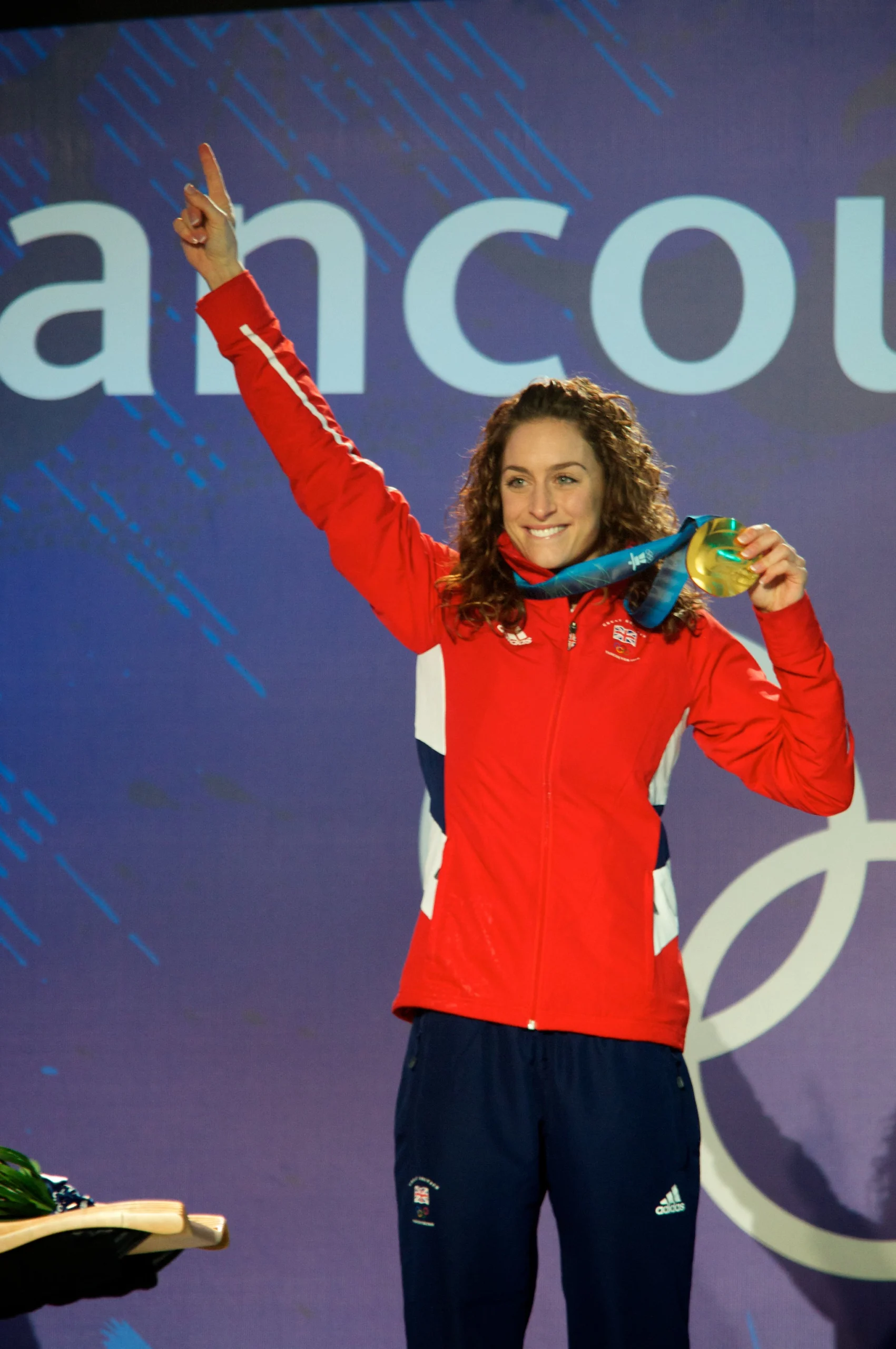 An athlete on a medal podium raising a gold medal, photographed from the press area at a major sporting event