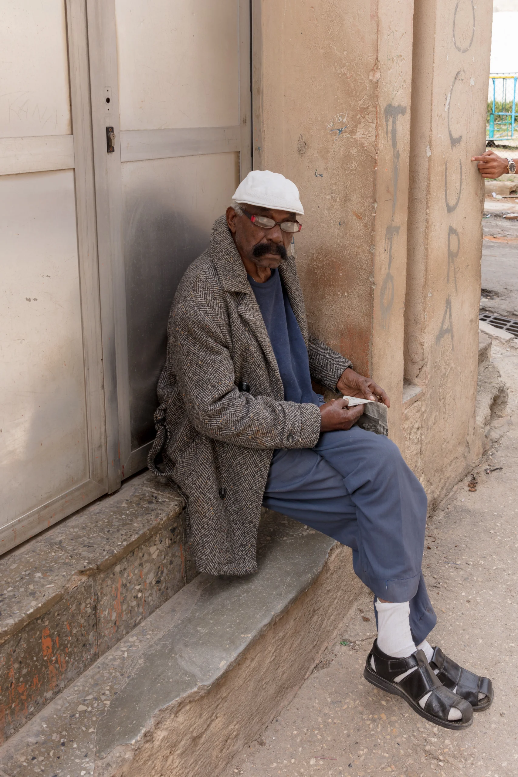 A street portrait of a man sitting in a doorway, photographed while traveling
