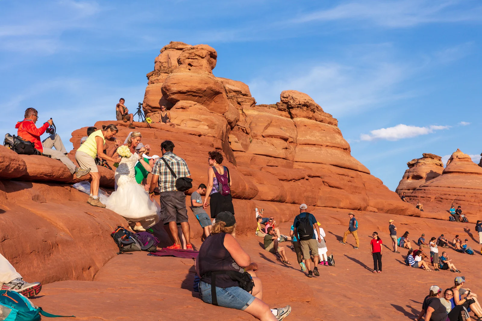 A wedding photographer and assistant working with a bride at a crowded public landmark, with tourists and hikers nearby