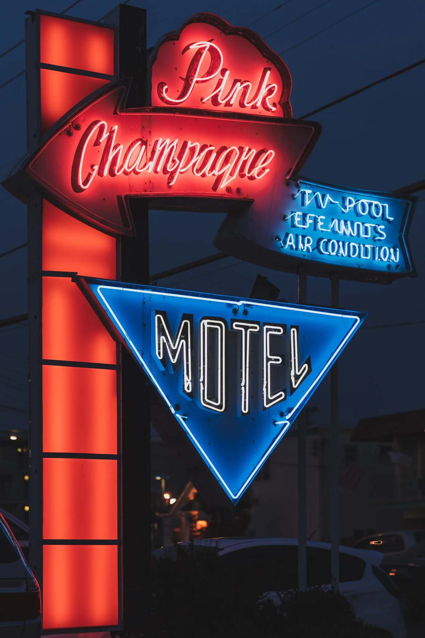 Vintage motel sign at dusk with glowing red neon script and a blue neon triangle outlined against a dark blue sky