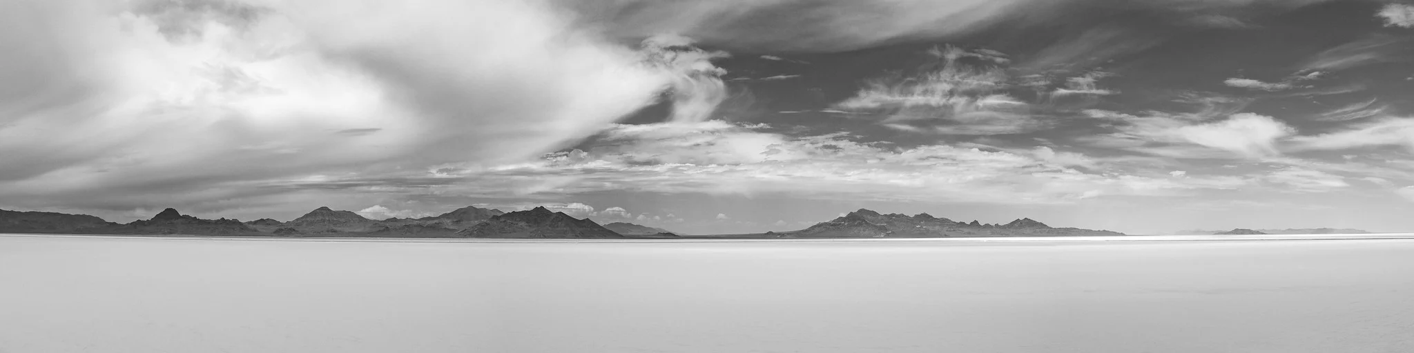 Flat white salt desert meeting a calm horizon under a wide sky, black and white