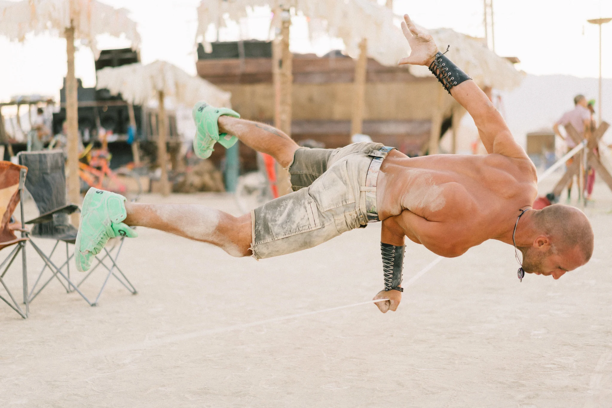 A slackliner holds a handstand at Burning Man, shot at f/1.8 so the tents and crowd behind him blur into soft shapes