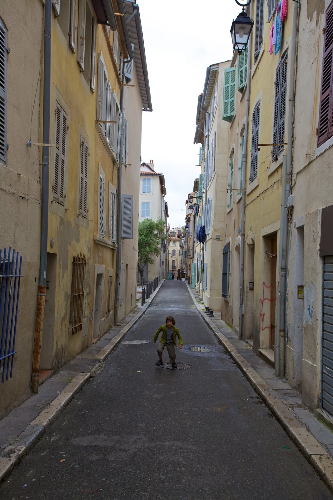 A boy running down a narrow, colorful alley in Marseille, France, framed by tall buildings on either side