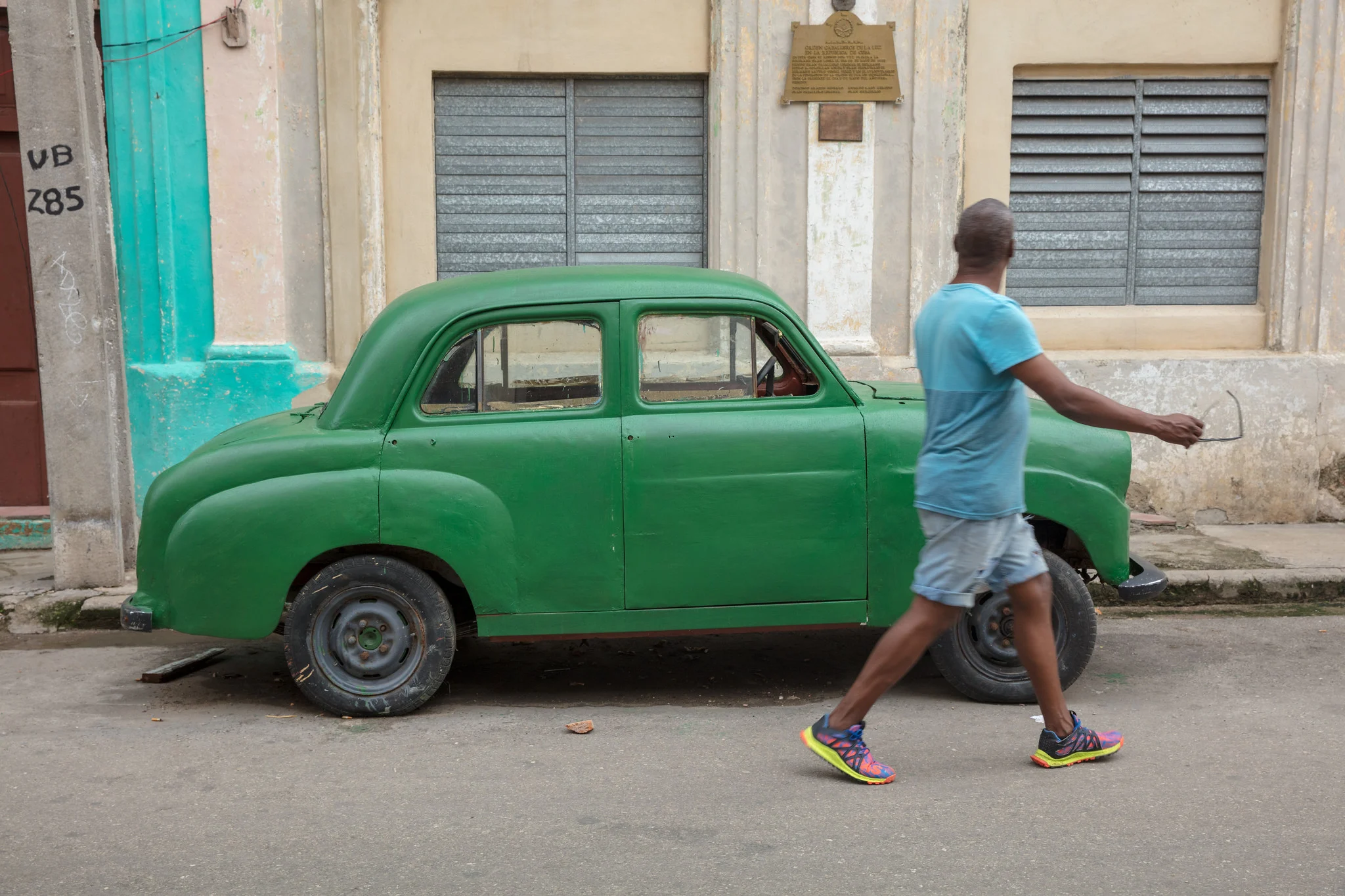 A man walks past a parked vintage green car on a street in Havana, Cuba