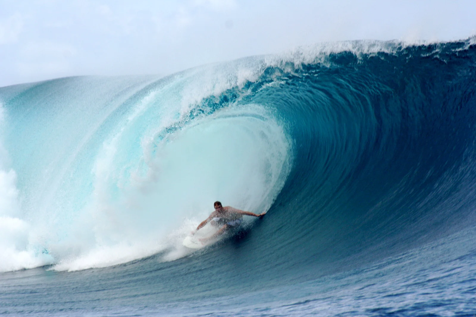 Surfer riding inside the barrel of a large breaking wave, spray frozen in mid-air