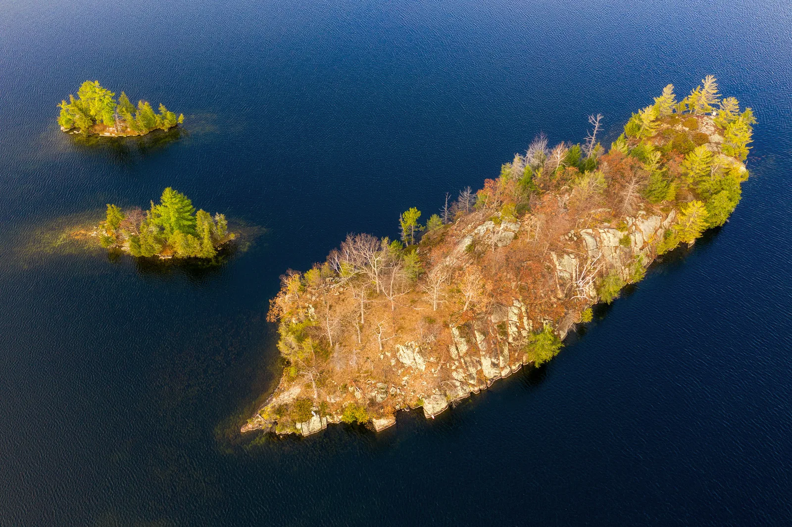 Aerial view of three wooded islands in dark blue water, two small ones at the left and one much larger rocky island stretching across the right