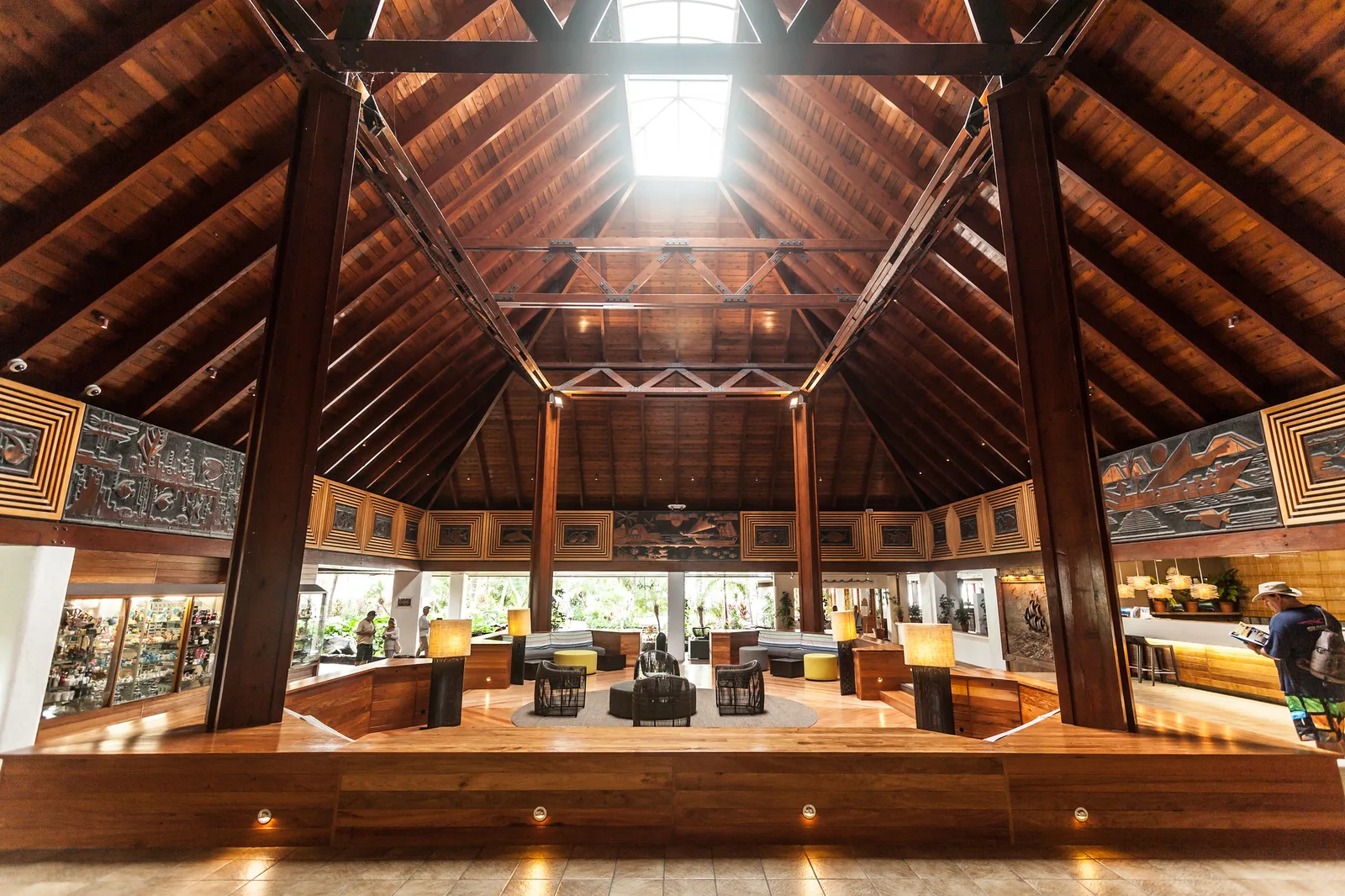 A wide view of an open hotel lobby under a tall timber roof with a skylight, heavy wooden posts, display cases and seating on a polished wooden floor