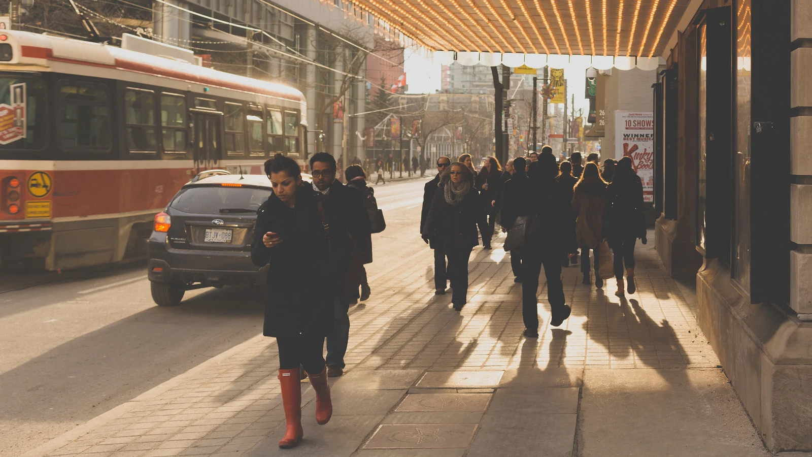 Commuters walking down a sunlit sidewalk in Toronto, backlit with long shadows stretching toward the camera