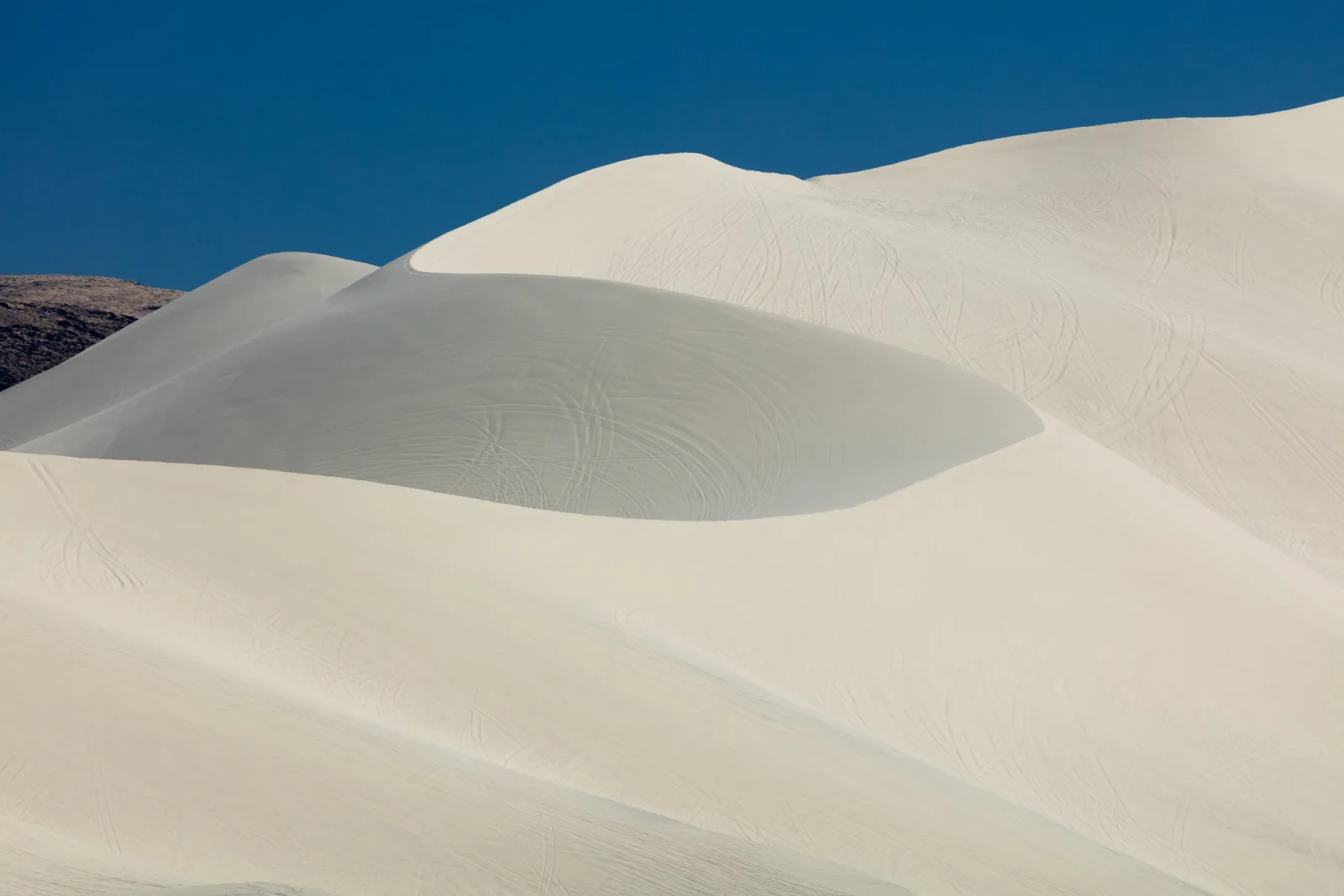 Smooth white sand dunes under a deep blue sky in bright sun, with soft shadows along the curves of the dunes