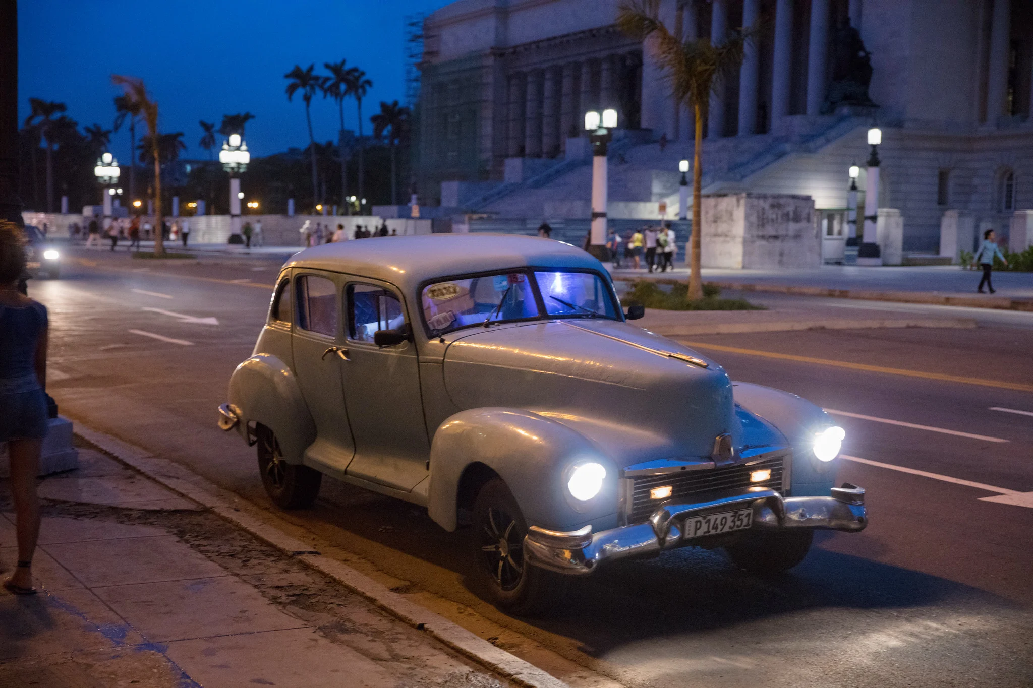 A vintage car parked on a Havana street at night, lit by its own headlights and streetlights.