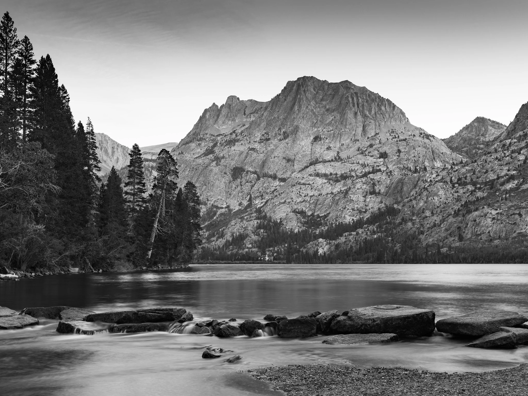A mountain lake with sharp rocks and mountains but silky, blurred moving water from a long exposure.