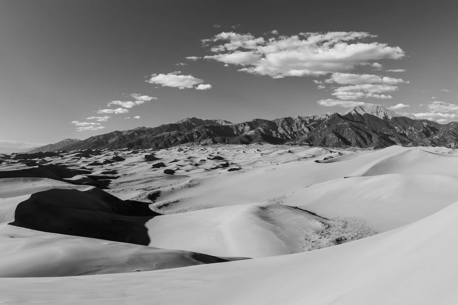 Bright black and white view of pale sand dunes below dark mountains and white clouds