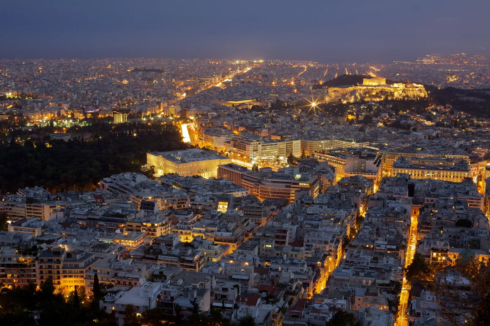 Athens at night seen from a hill, with warm streetlights across the city and the lit Acropolis on the skyline