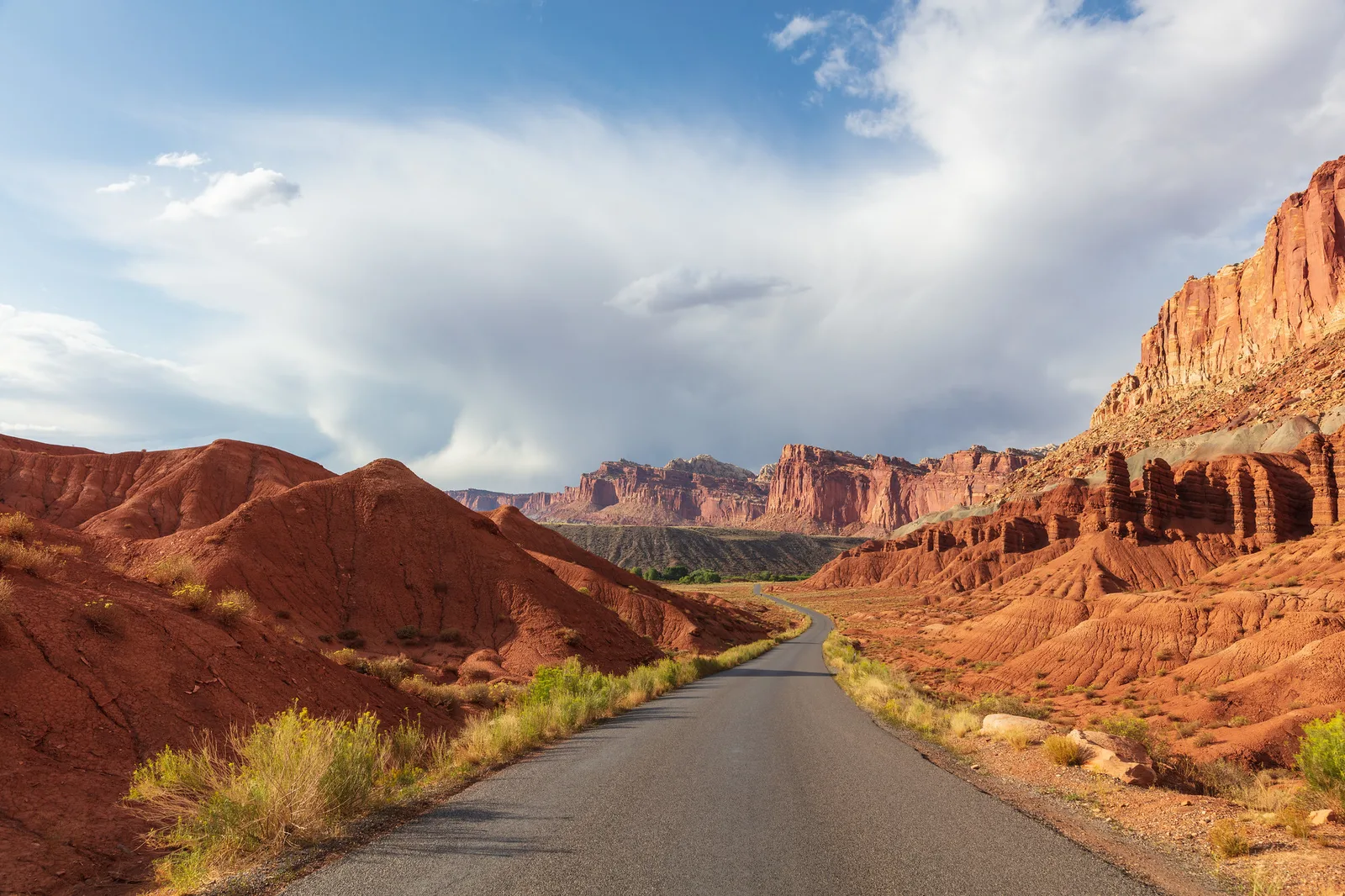 A road winding between red rock canyon walls under a blue sky with white clouds, a scene where small edits to color and contrast are easy to compare