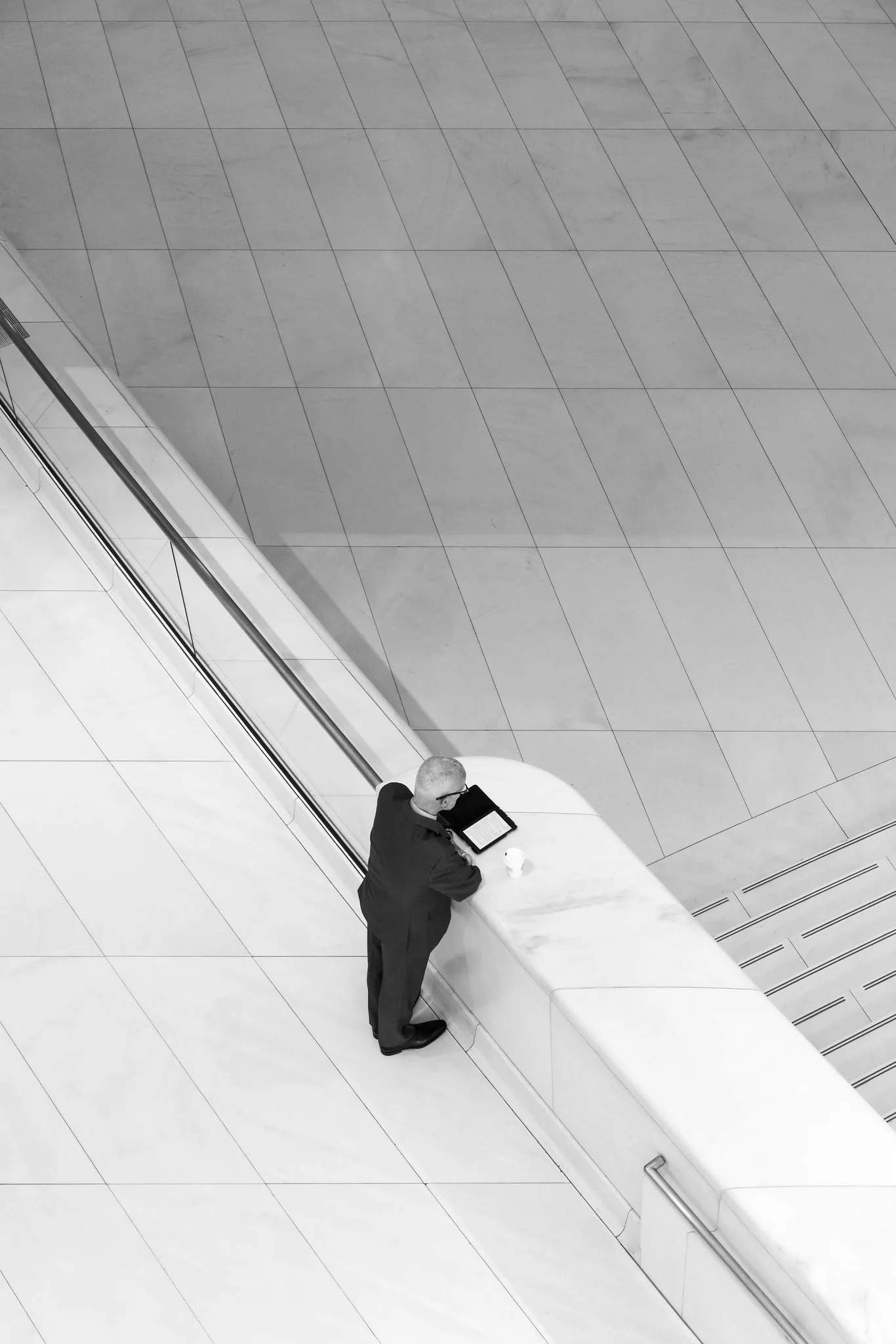 A small figure reading on a white marble staircase in a vast modern hall, shot from above so the face is not visible