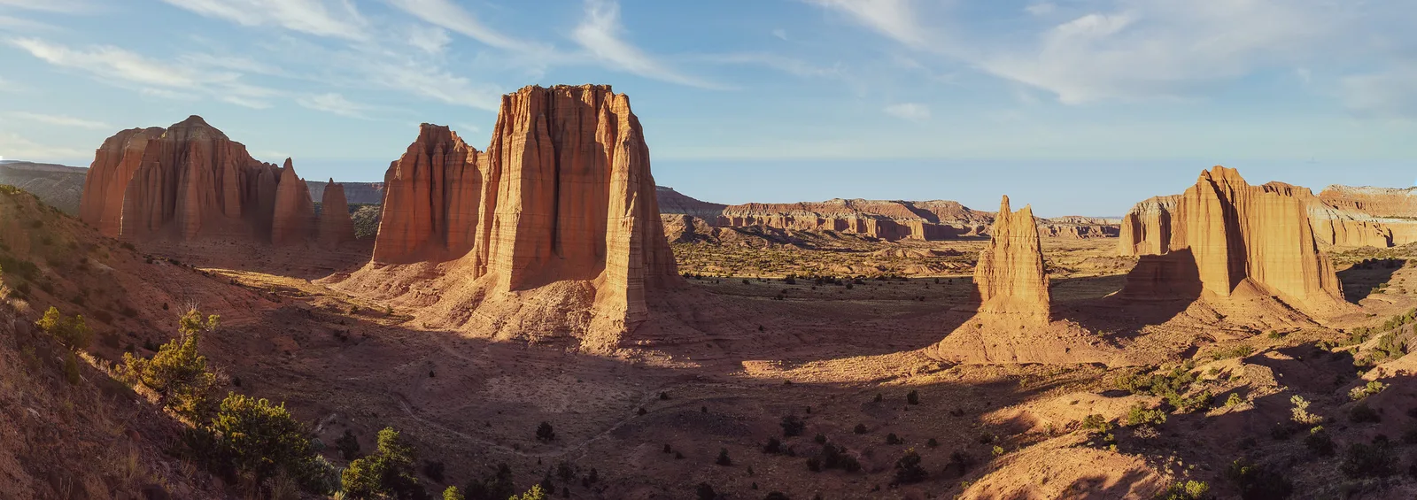 A wider view of the same desert valley, with sandstone towers and cliffs under a blue sky with light clouds