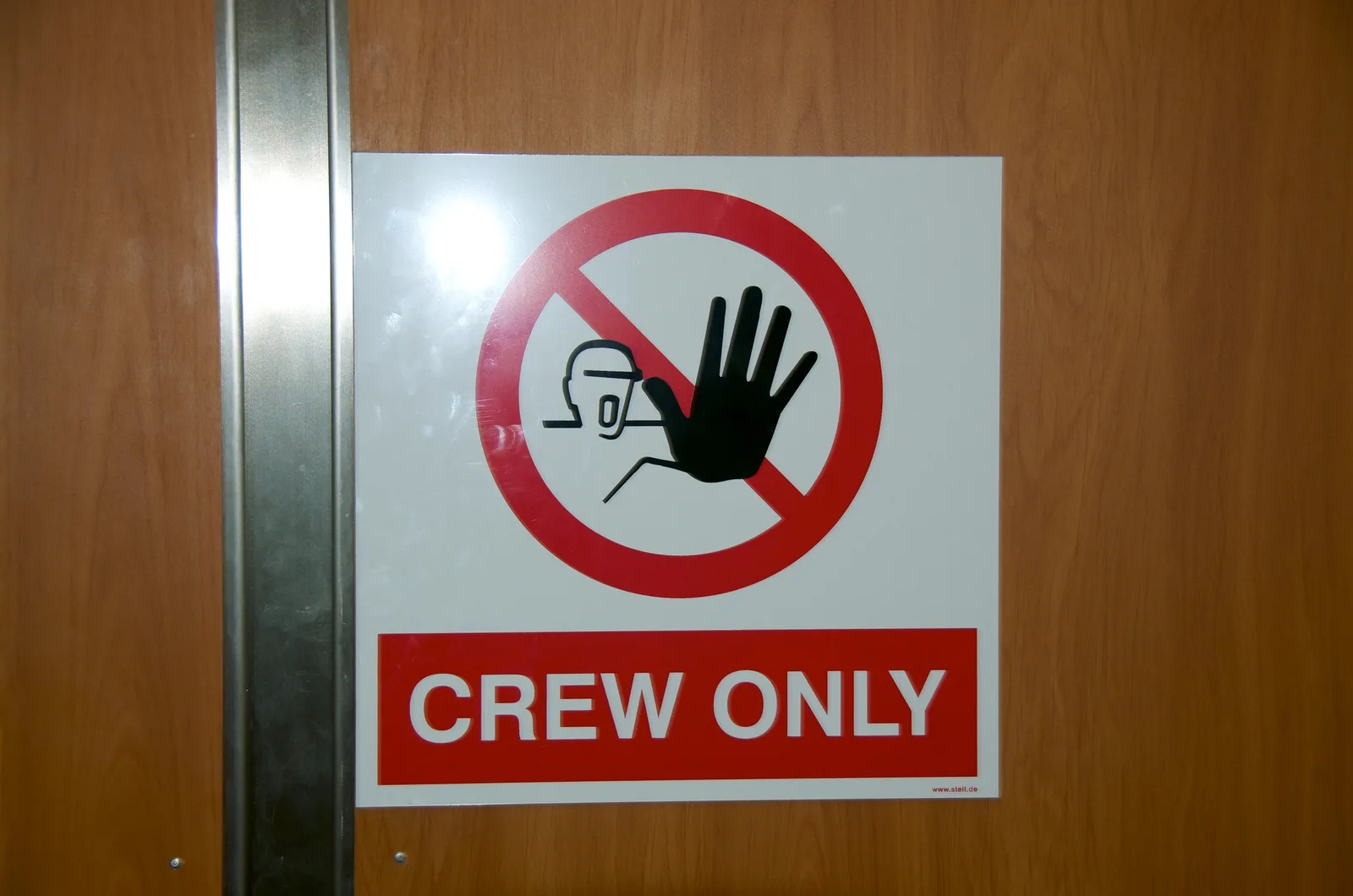 A red and white Crew Only sign with a raised-hand symbol fixed to a wooden door beside a metal frame.