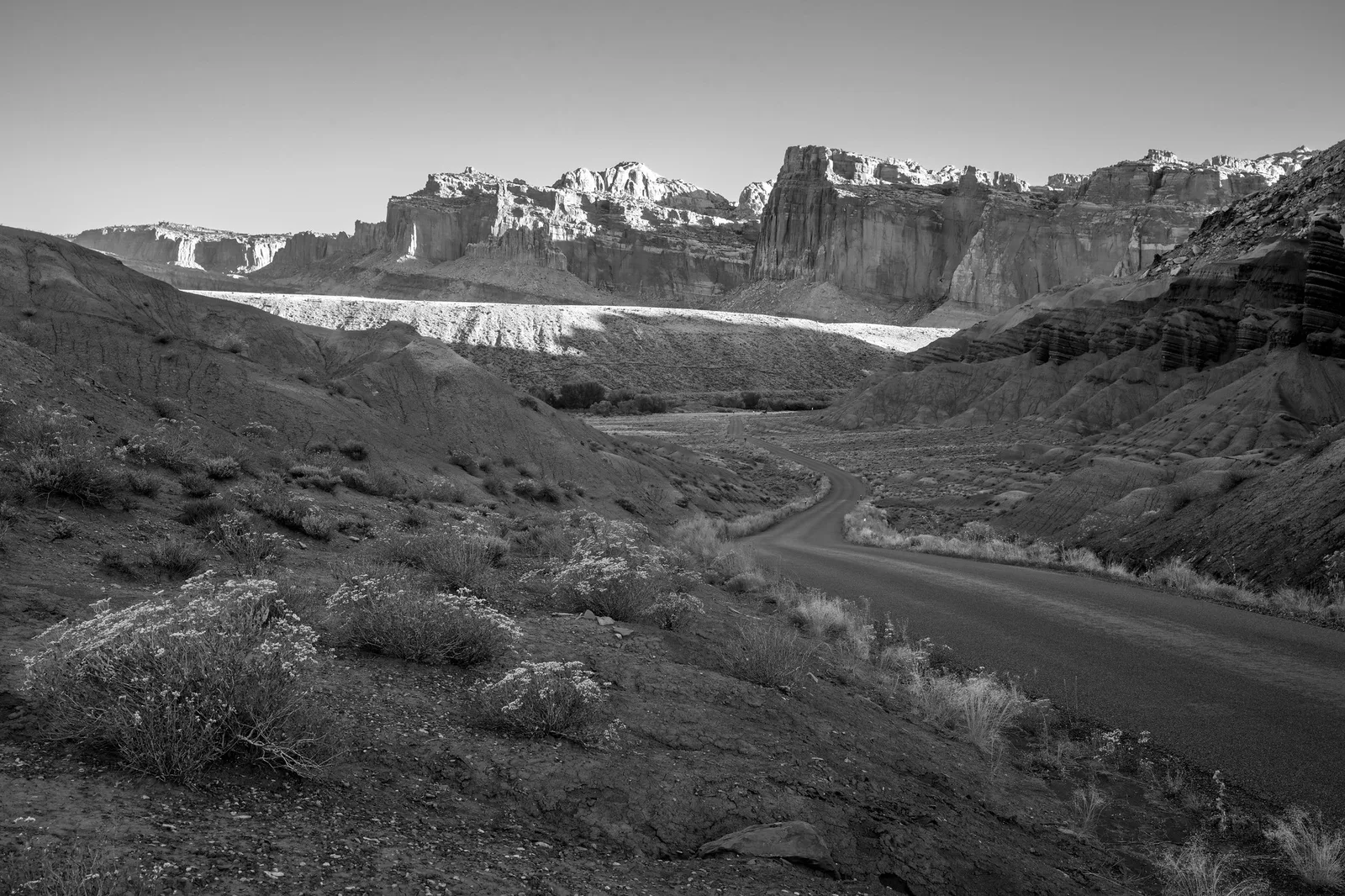 Black and white view of a road curving through rolling hills toward jagged mountain peaks