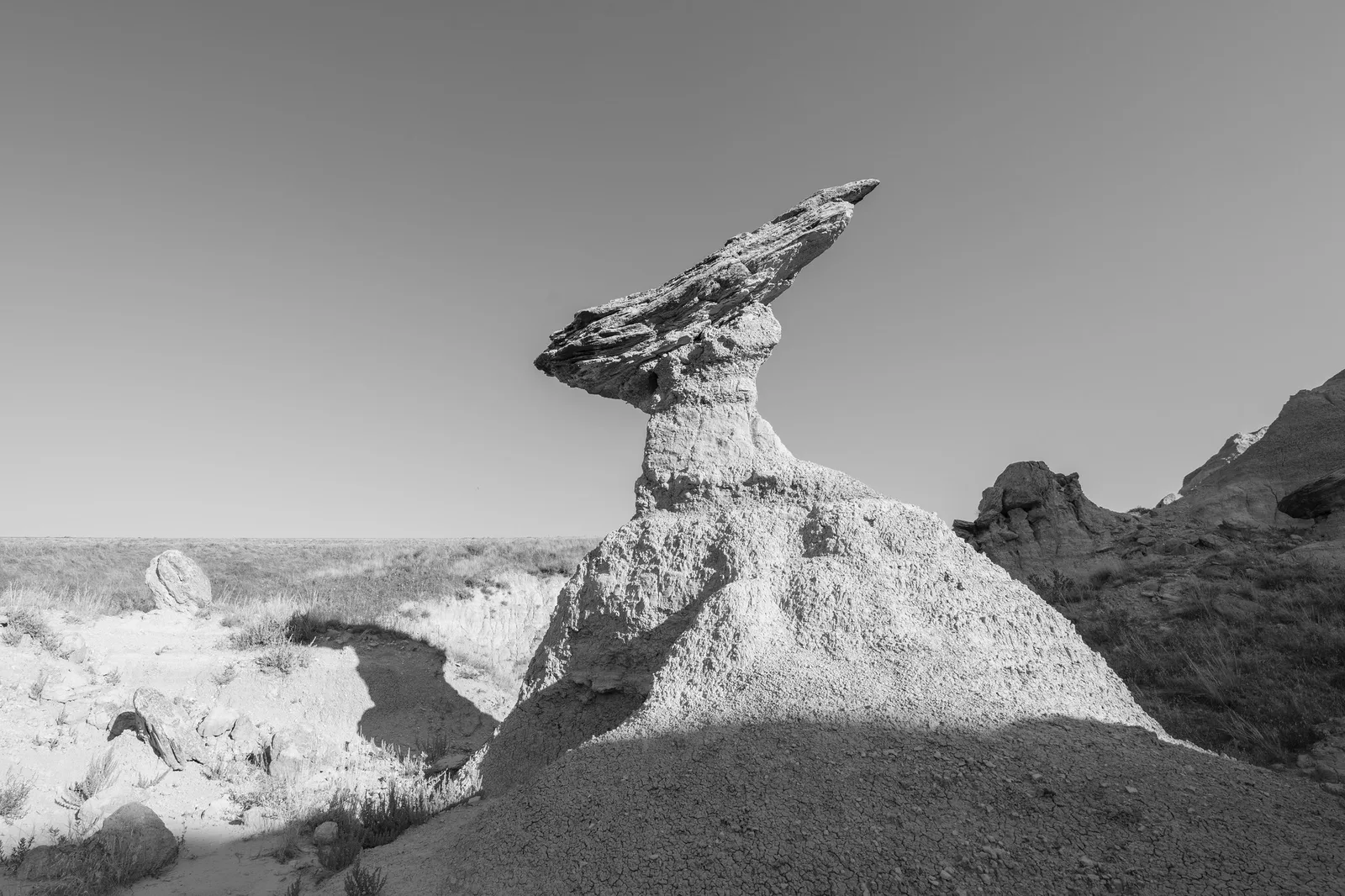 Black and white photo of a balanced cap rock on a pale eroded pillar in harsh desert light