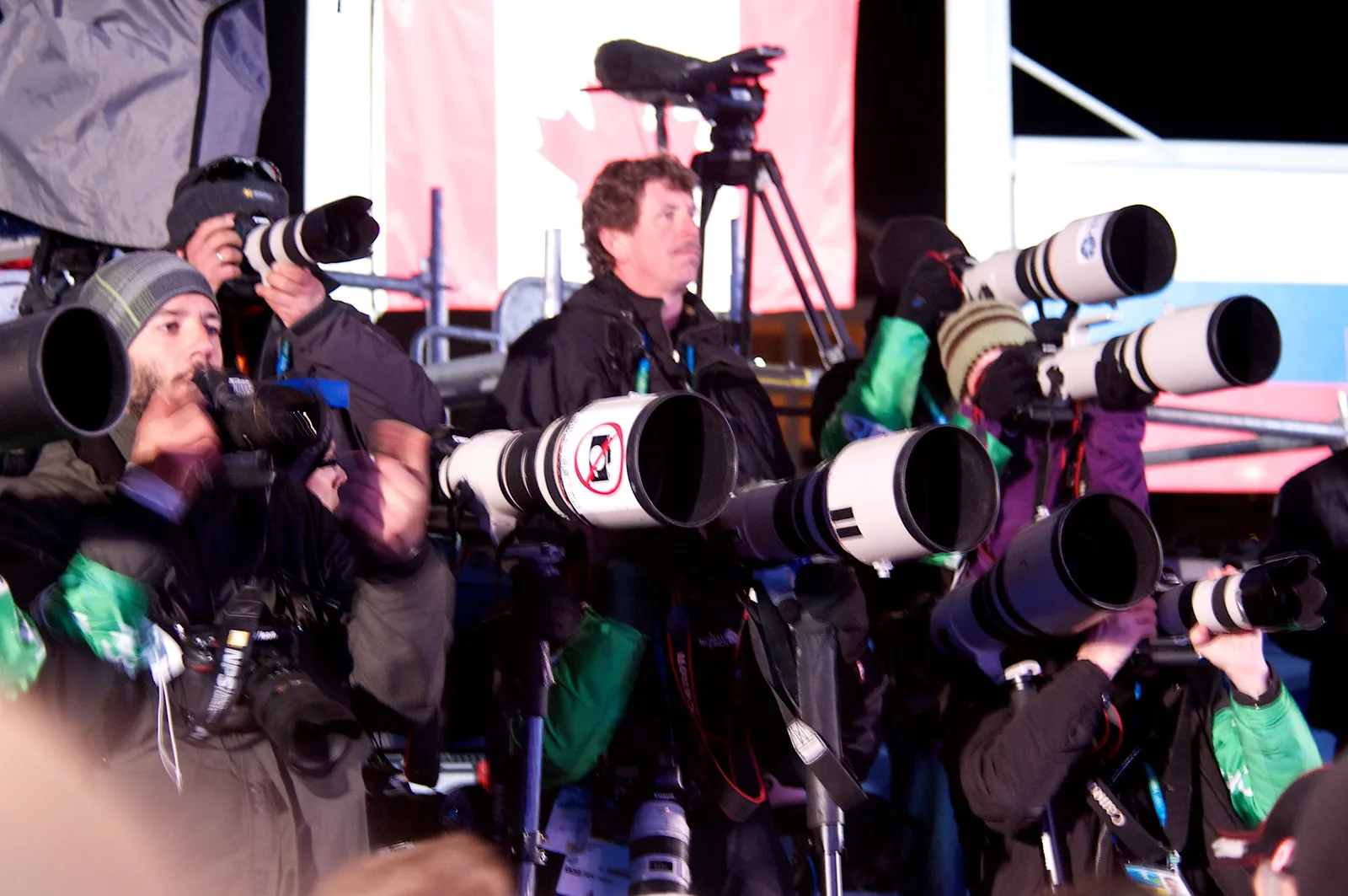 A pack of press photographers with long lenses lined up at a public event, all aiming at the same subject