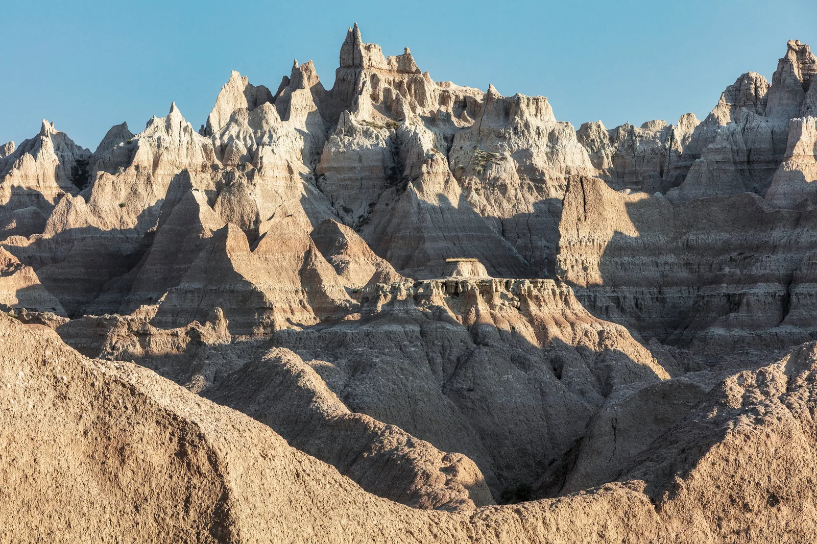 Layered badlands rock formations in pale cream, grey and ochre under clear light