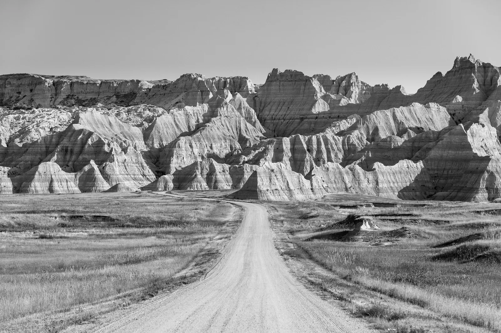 Black and white photo of a road leading straight toward jagged badlands peaks, an example of a consistent monochrome editing style
