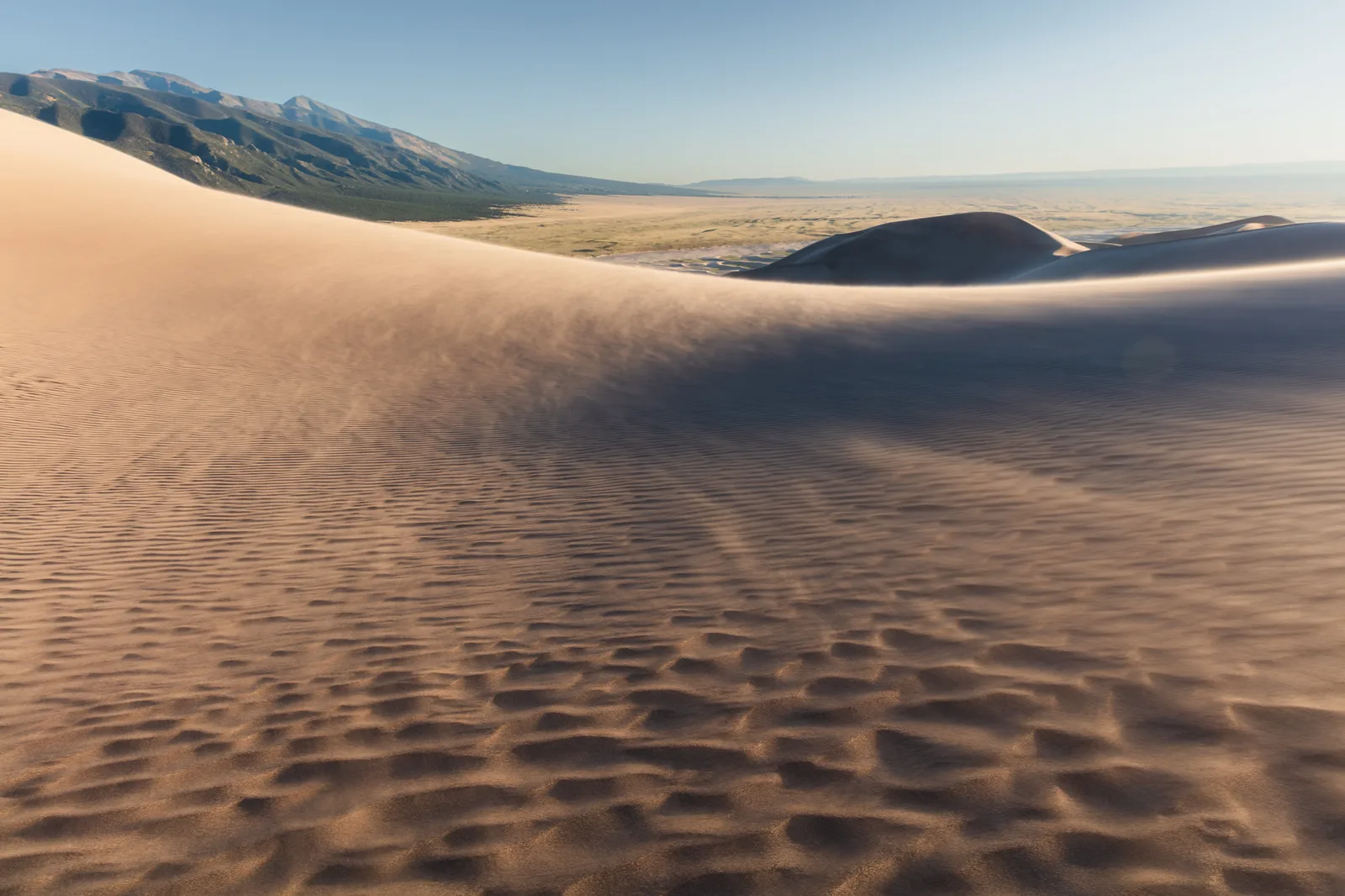 Soft light grading gently across rippled sand dunes, bright in one area and fading smoothly into shade, like light feathered across a subject