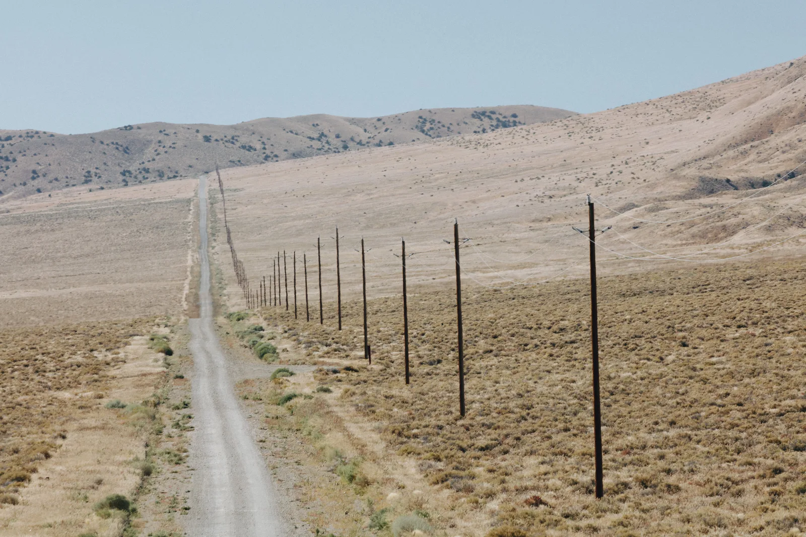 A long dirt road running into hills beside a line of wooden telephone poles, the old way of sending a signal over distance