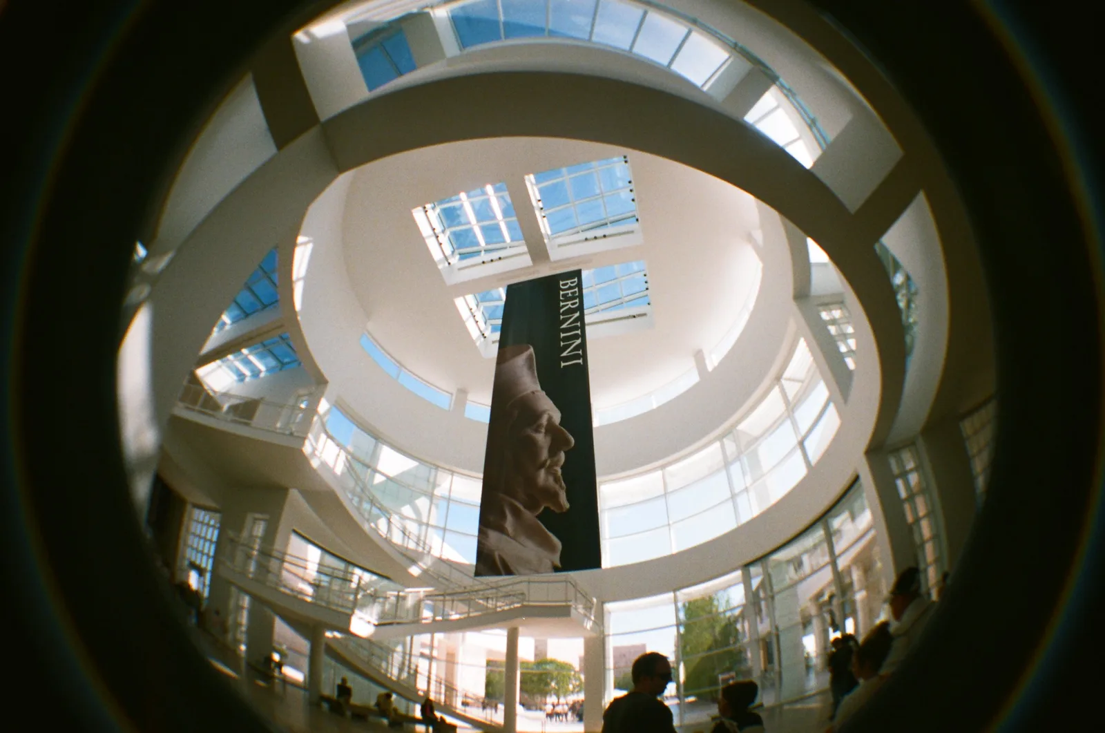 Fisheye film photo looking up into a round white museum atrium with skylights and a tall hanging banner
